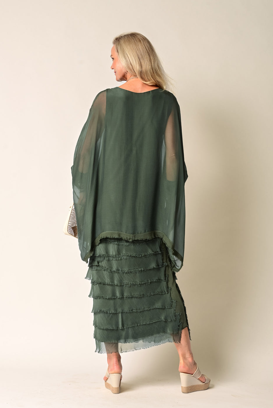 Woman wearing a green layered dress against a beige background