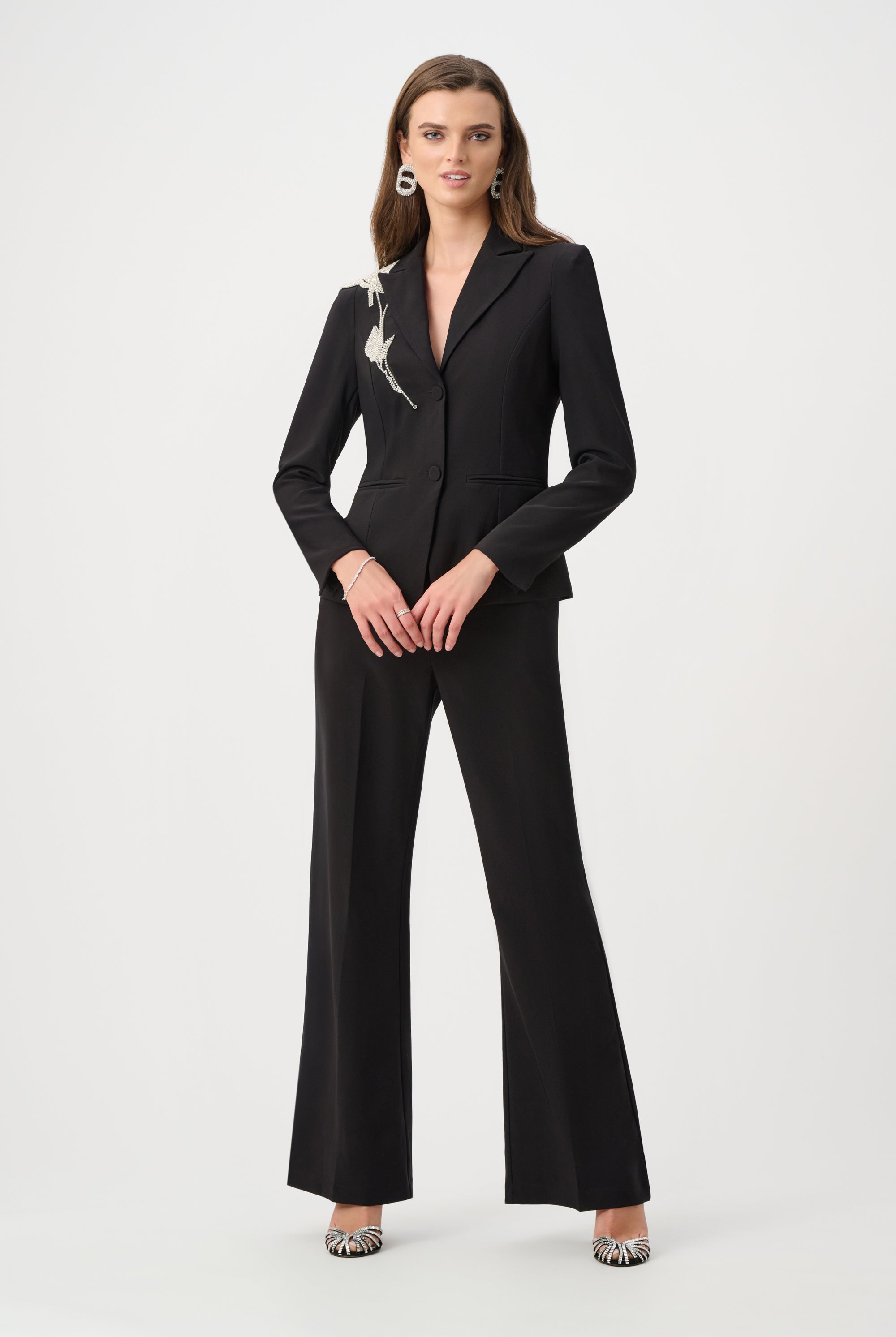 women wearing black pants and black blazer with rhinestones on shoulder on plain white background