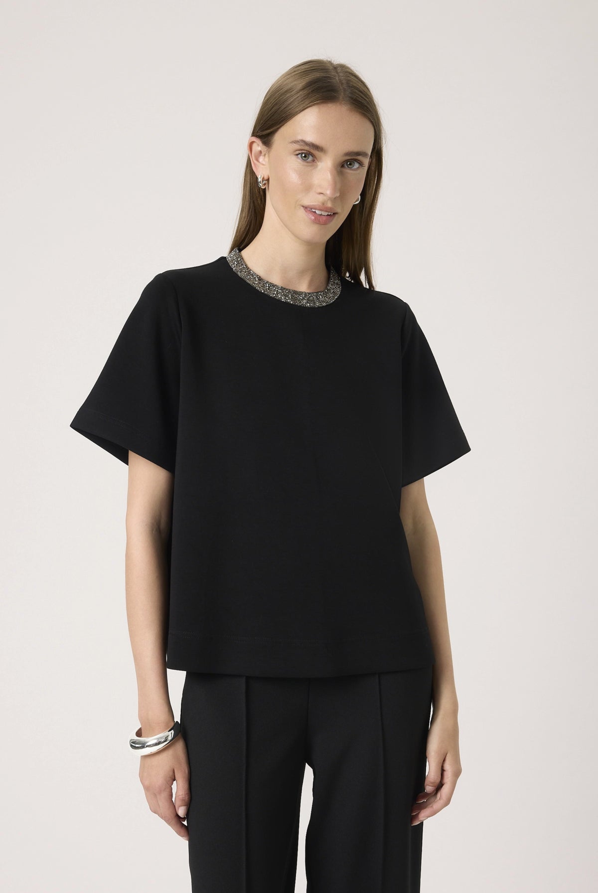 Woman wearing a black top with a sparkle neckline against a white background