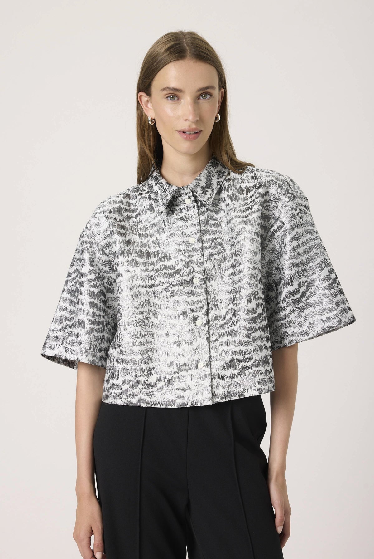 Woman wearing a patterned blouse and black pants against a light background