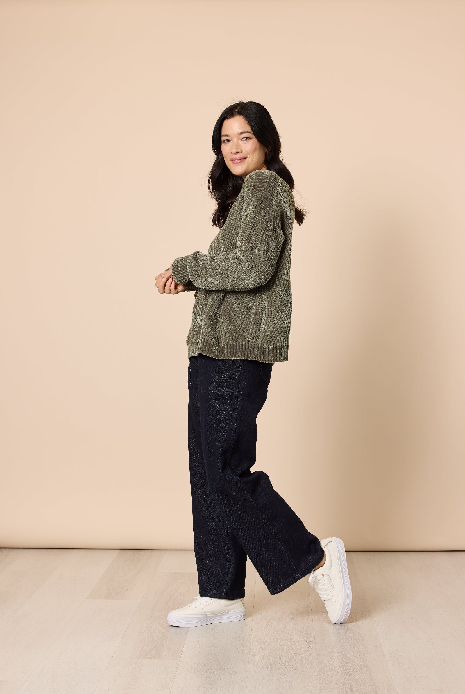 Woman wearing a green sweater and black pants against a beige background