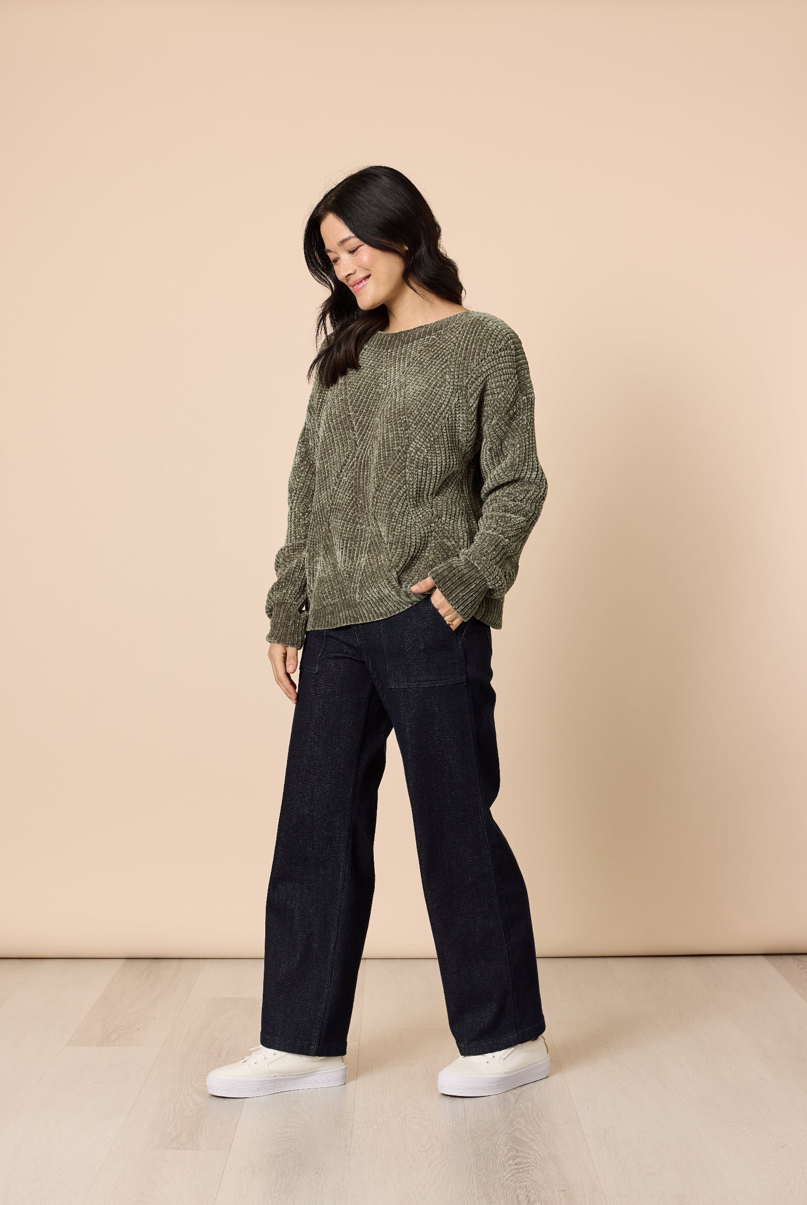Woman wearing a green sweater and black pants against a beige background
