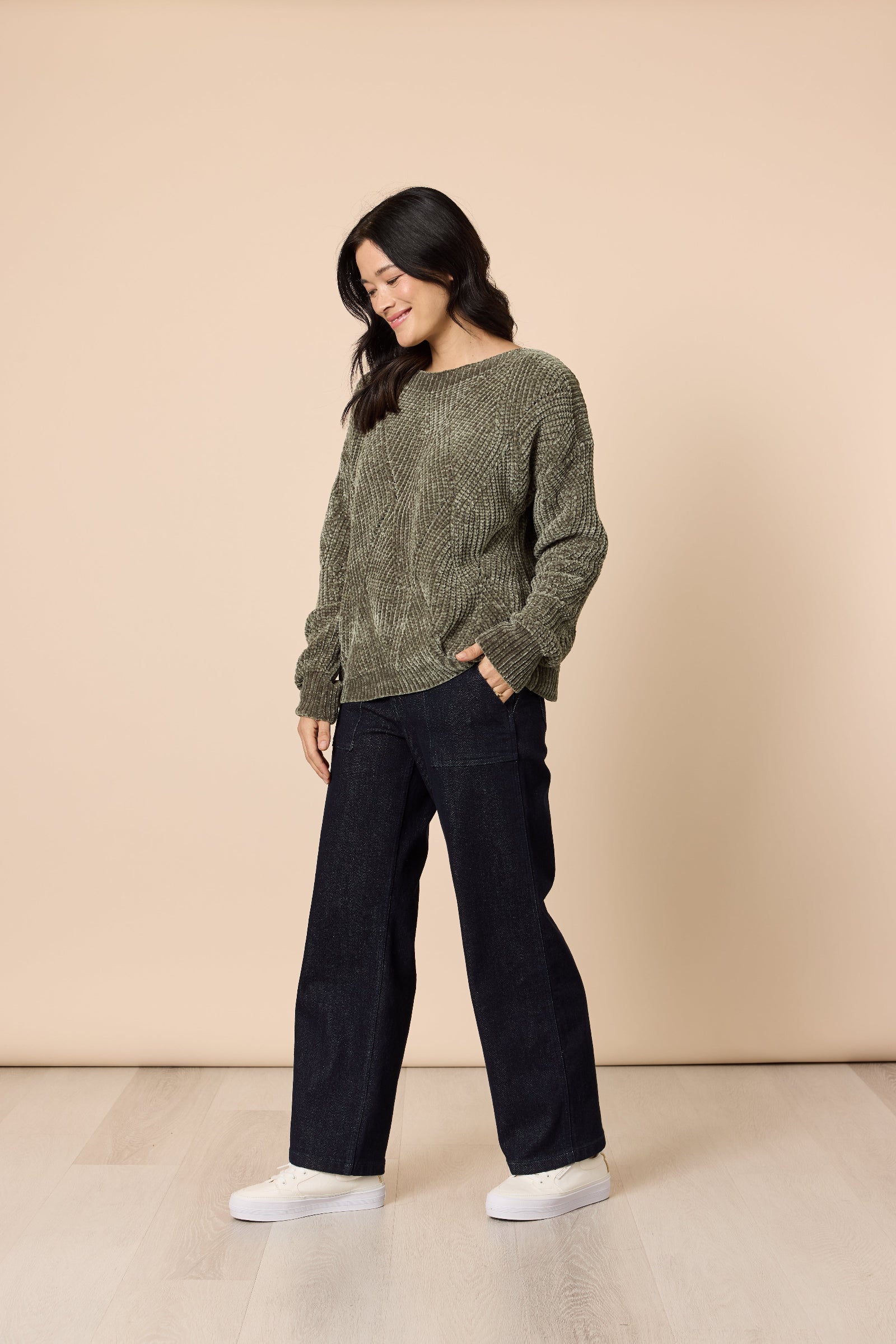 Woman wearing a green sweater and black pants against a beige background