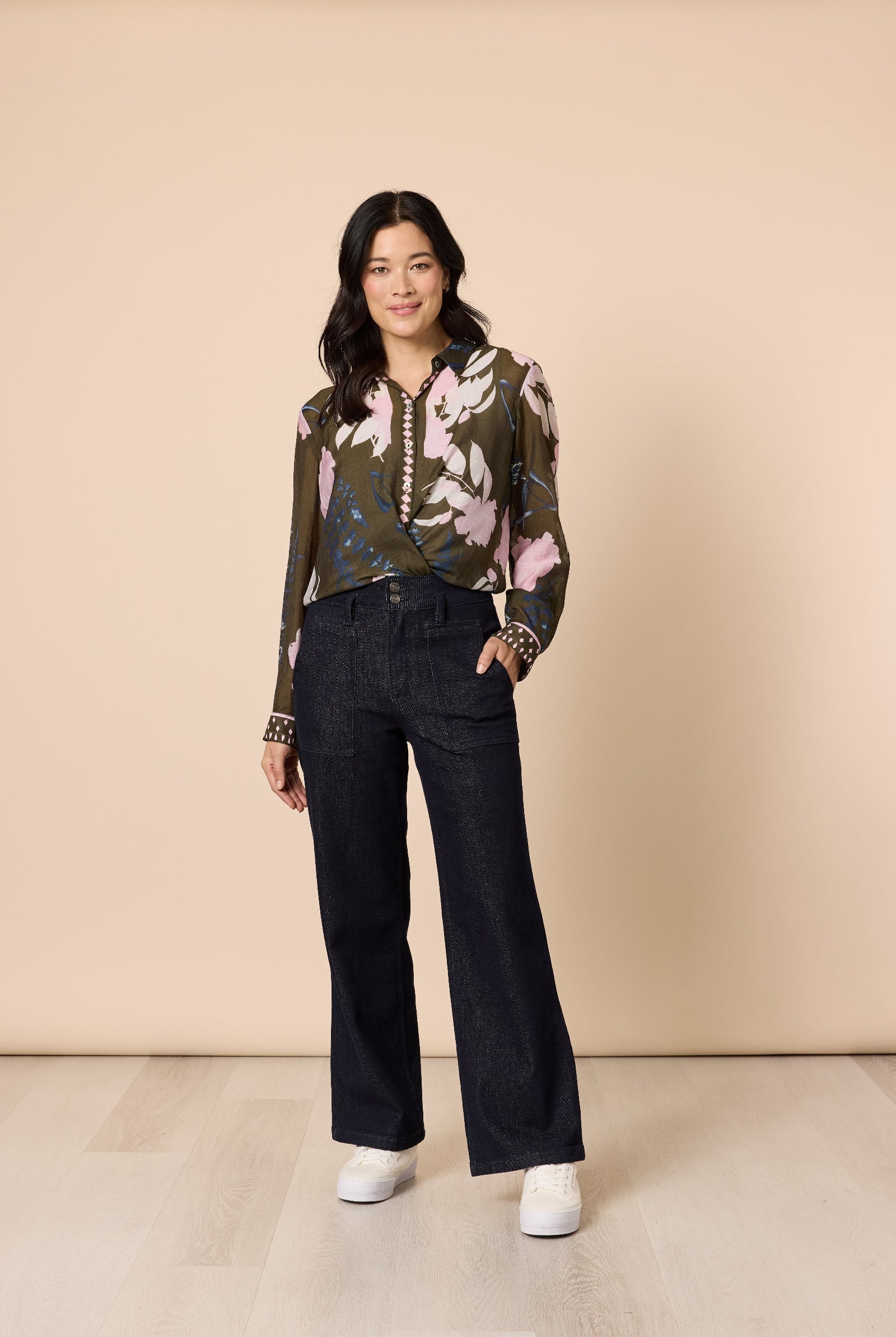 Woman wearing a floral blouse and black pants against a beige background