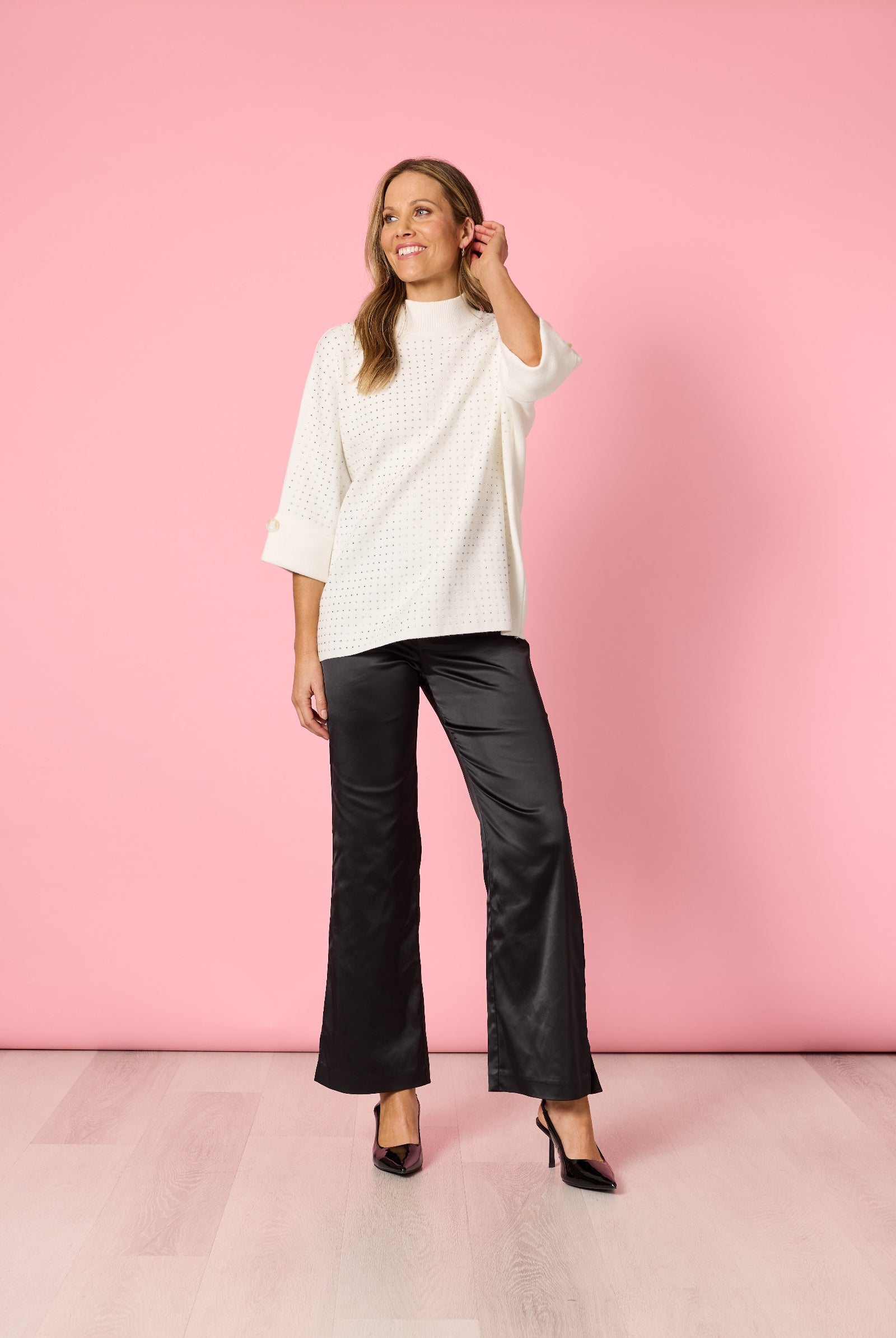 Woman wearing a white top and black pants against a pink background
