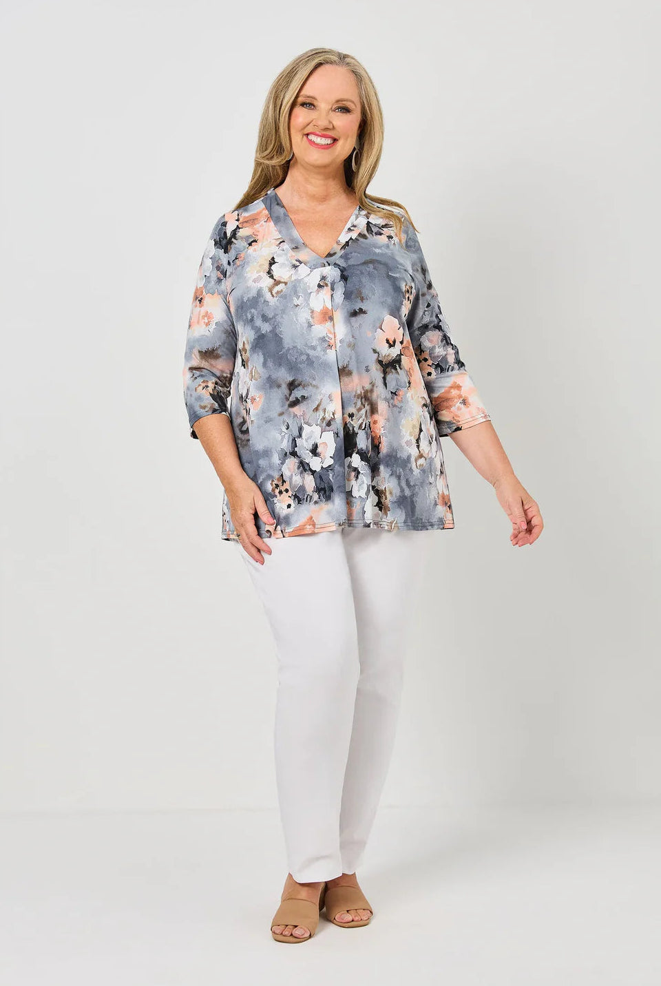 Woman wearing a floral blouse and white pants on a plain background
