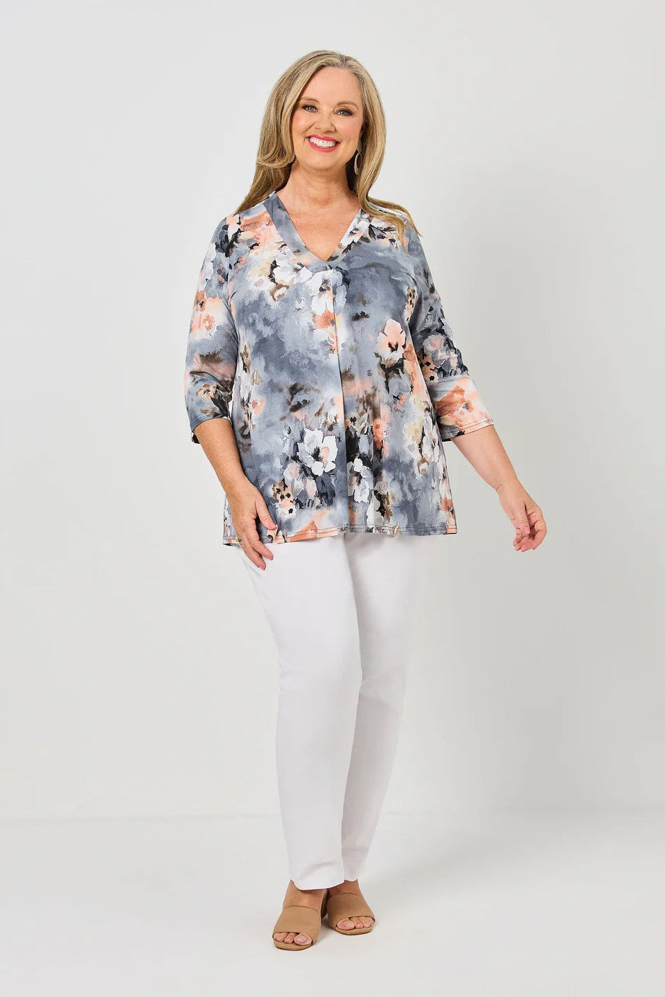 Woman wearing a floral blouse and white pants on a plain background