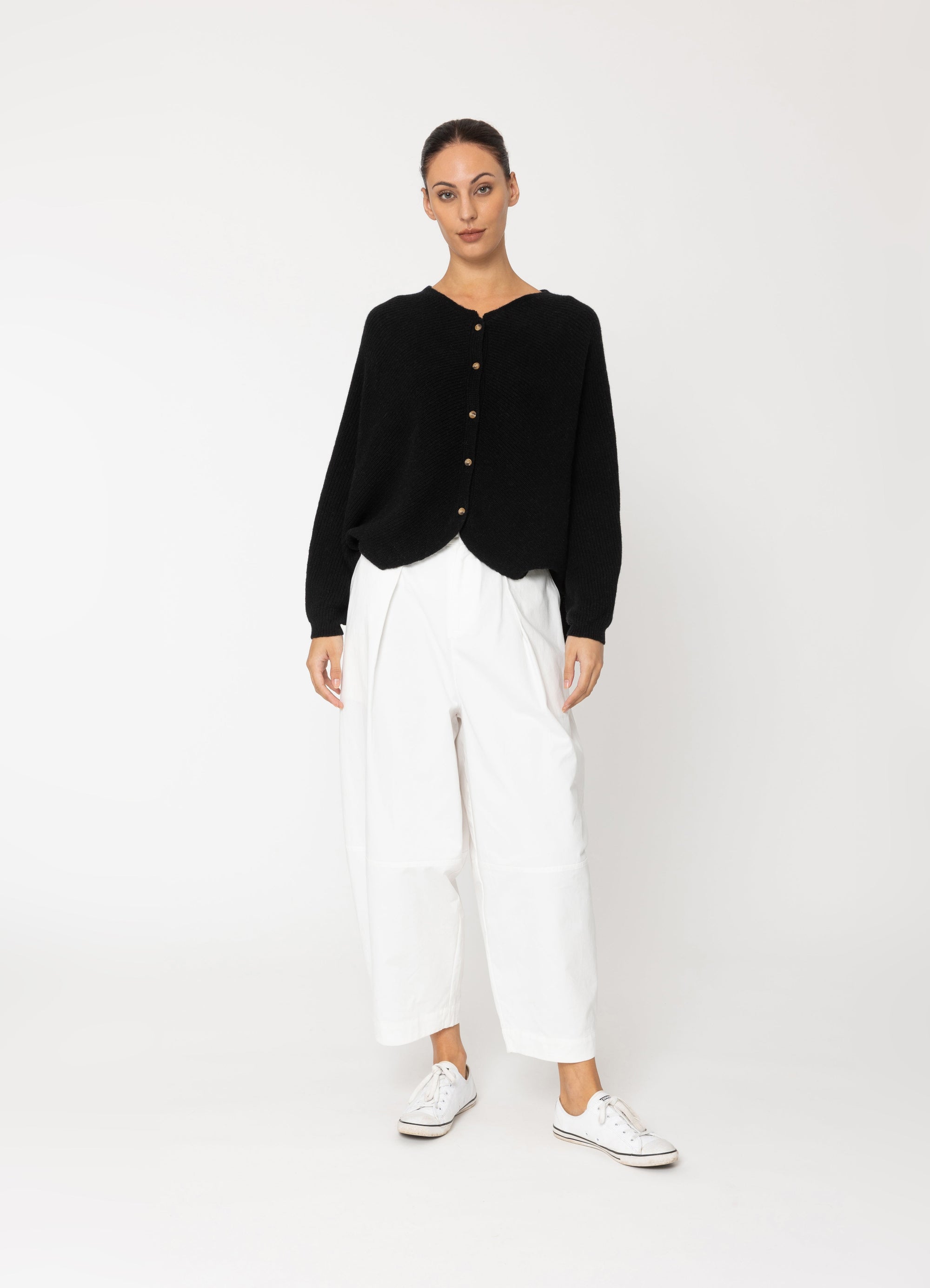 Person wearing a black cardigan, white pants, and white sneakers on a white background