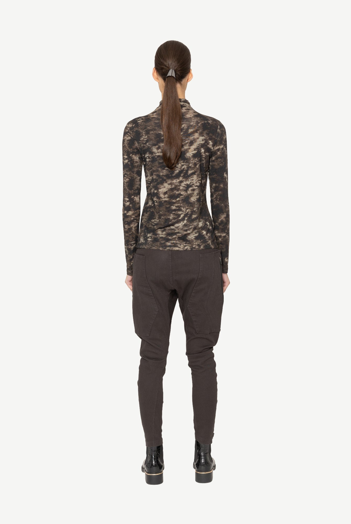 Person wearing a printed long-sleeve top and dark pants on a white background back angle