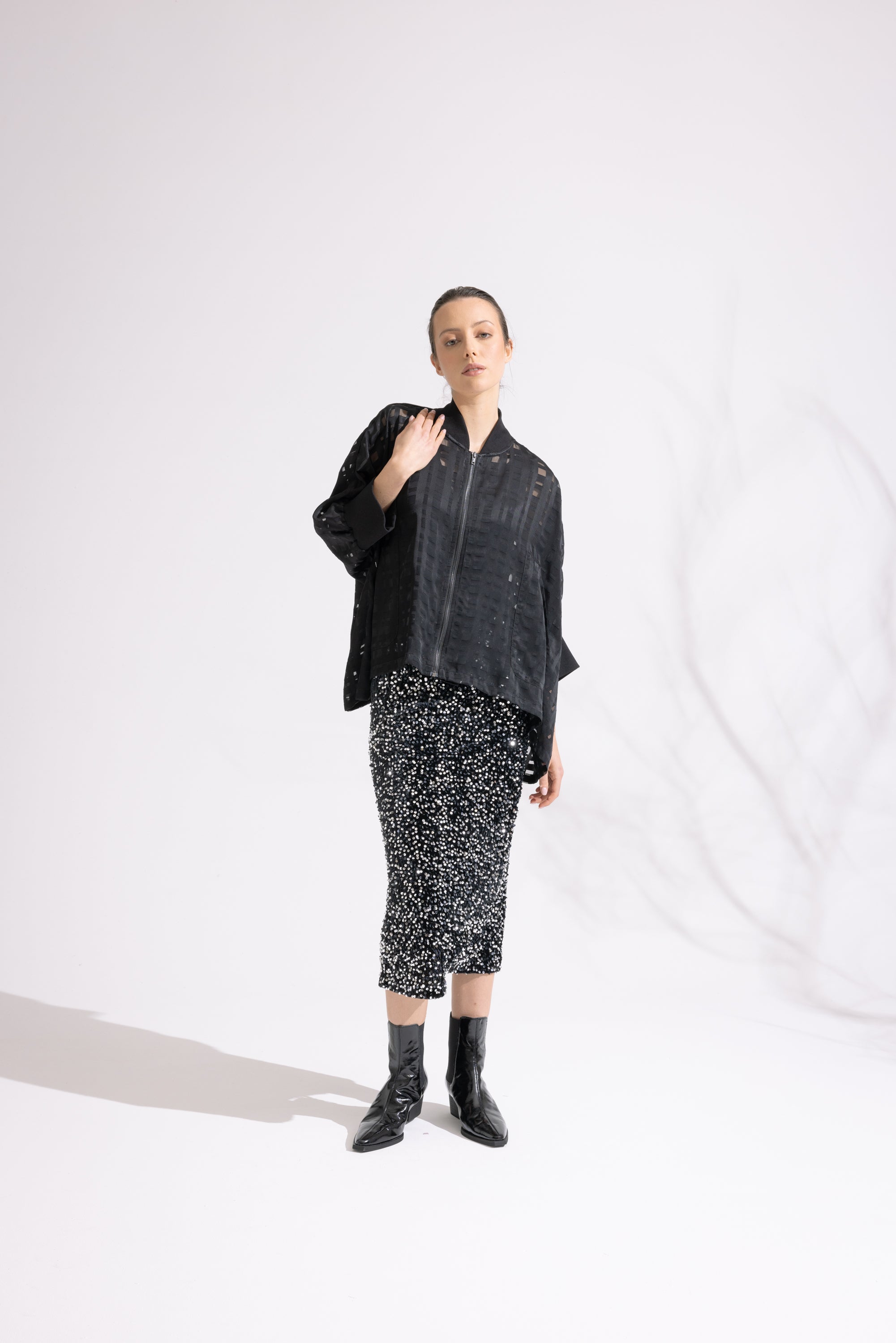 Person wearing a black jacket and patterned skirt on a white background