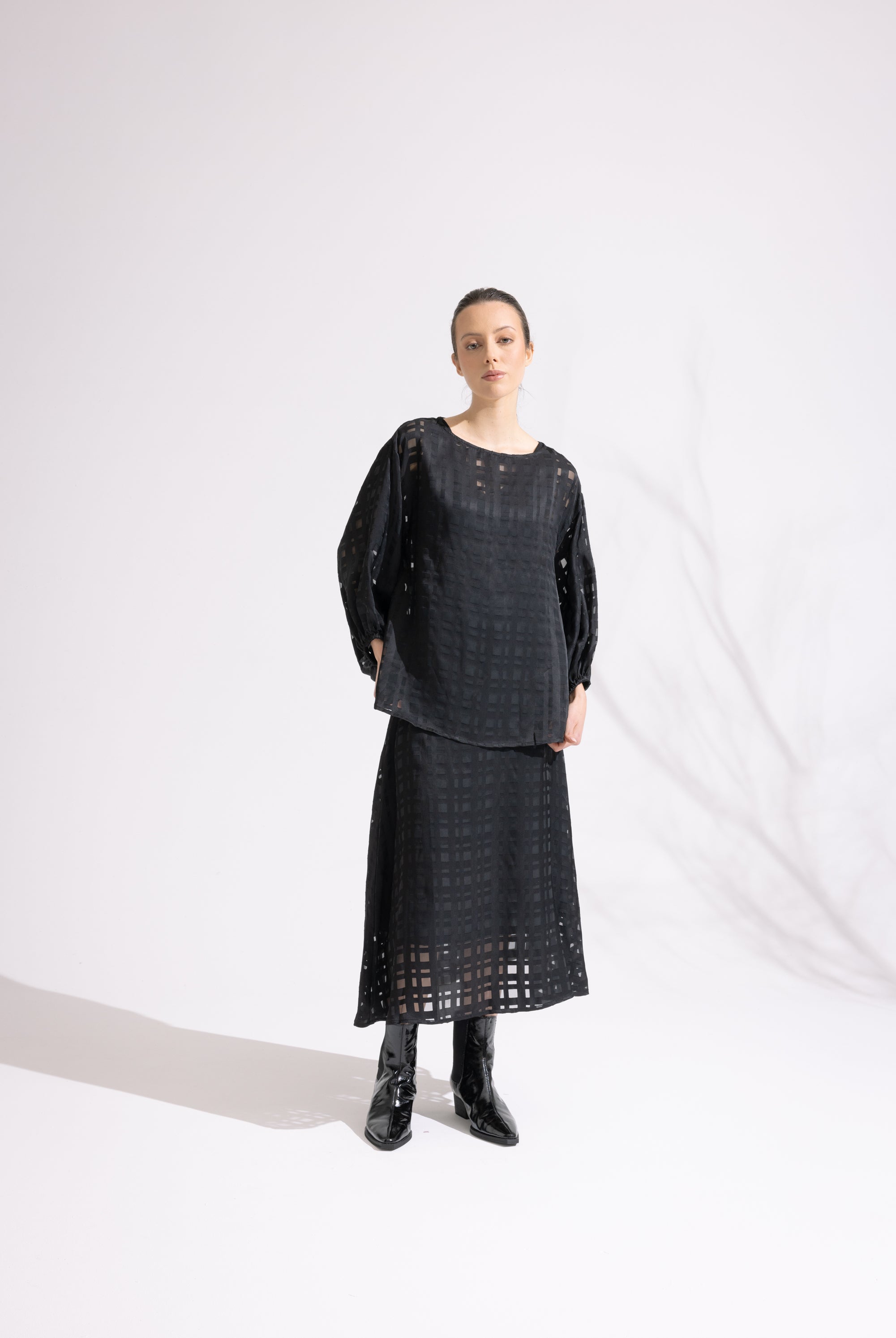 Person wearing a black outfit with a patterned skirt on a white background