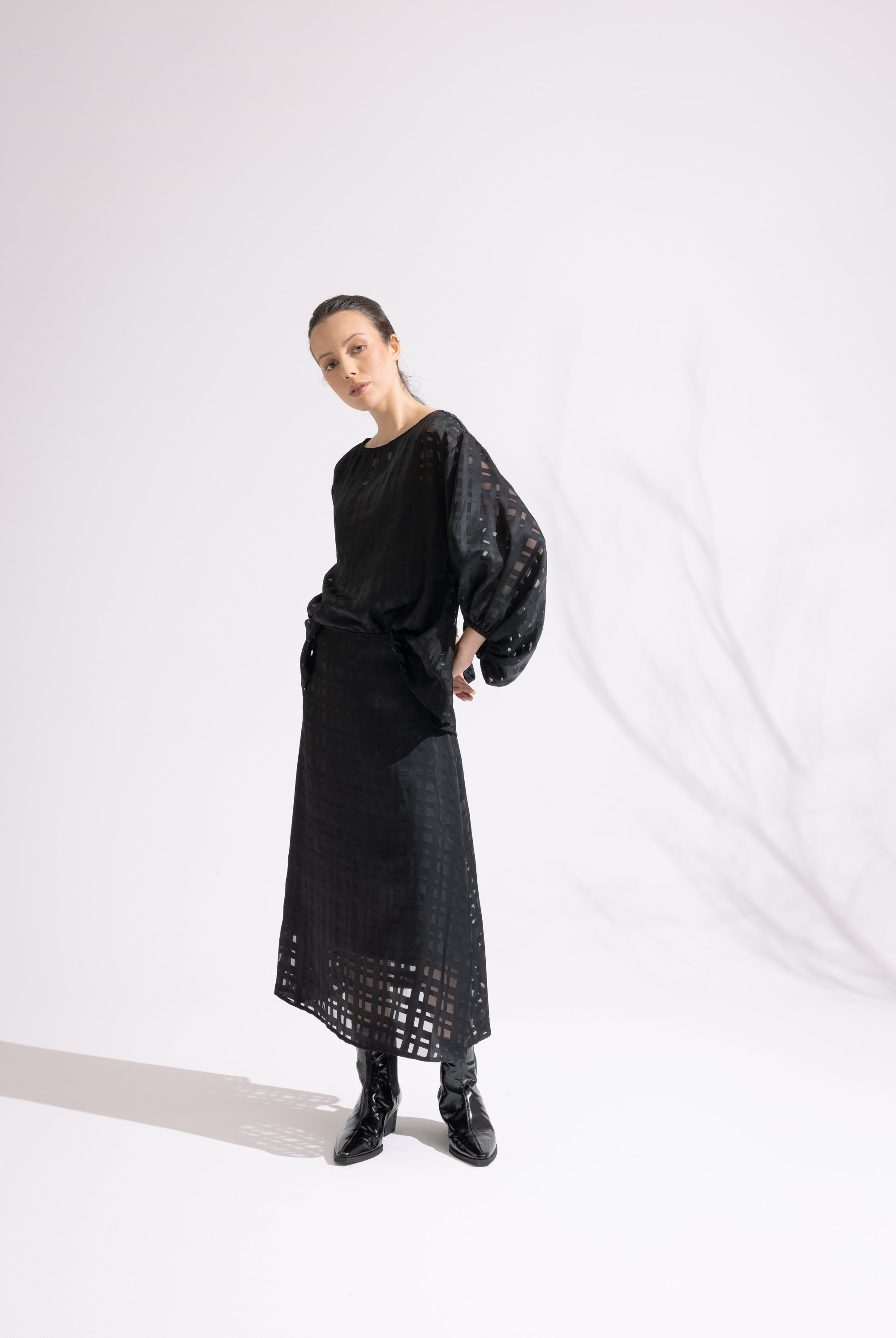 Person wearing a black outfit with a textured top and lace skirt against a white background