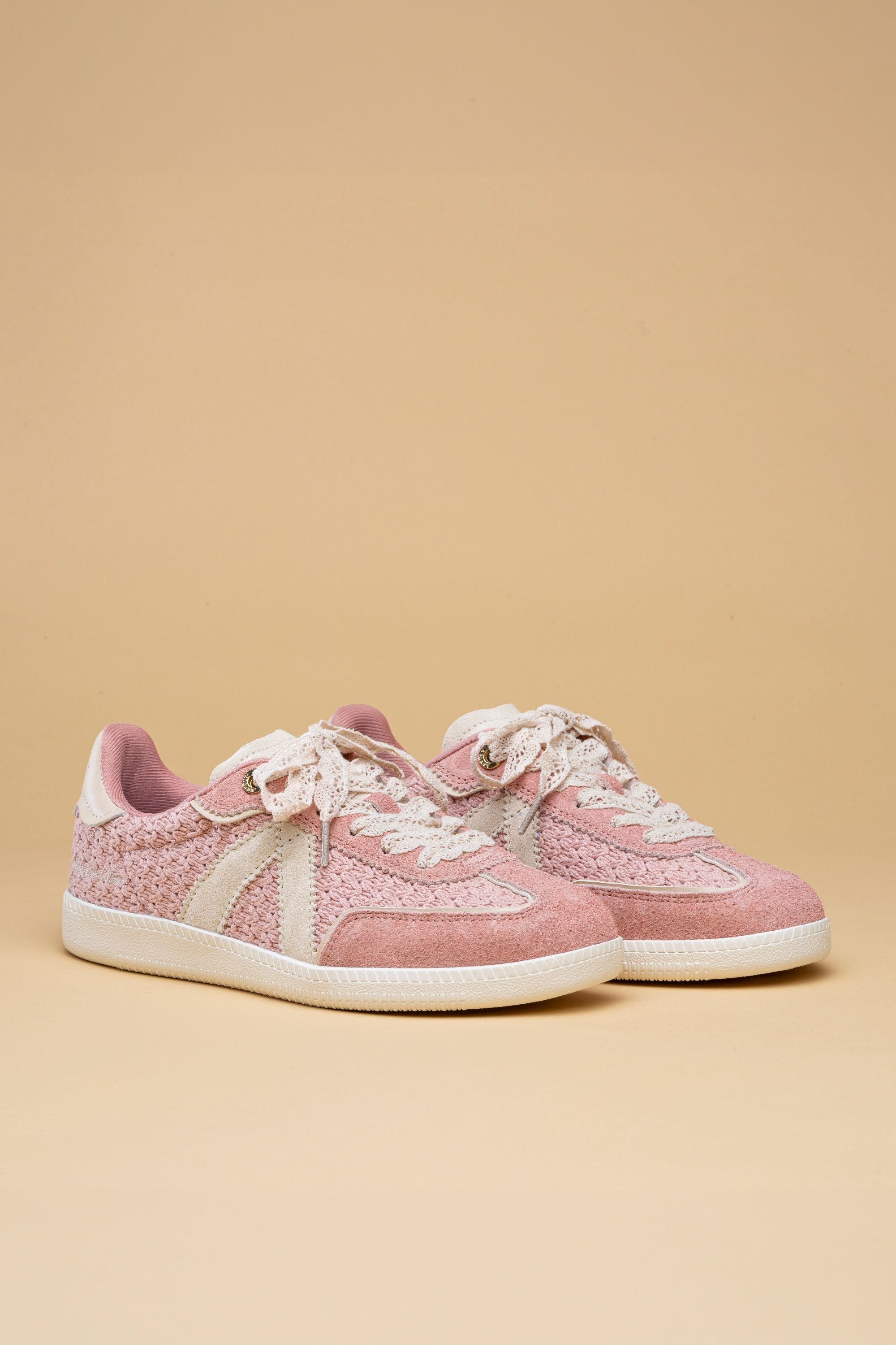 Pair of pink sneakers with white laces on a beige background