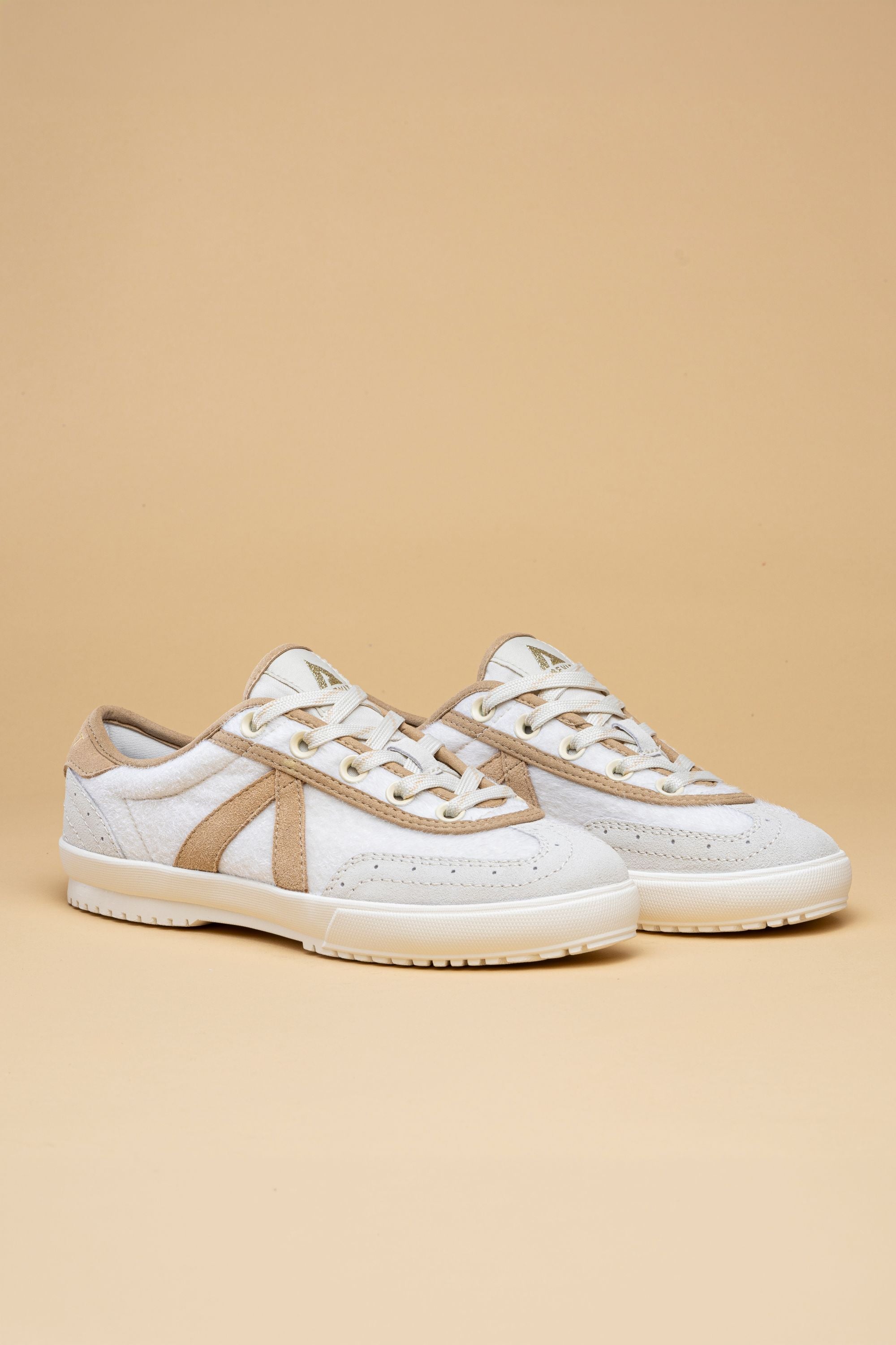 Pair of white sneakers with brown accents on a beige background