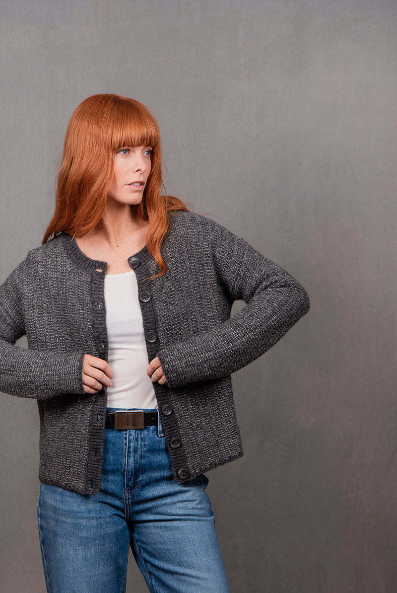 Woman wearing a gray textured cardigan over a white top and blue jeans against a gray background