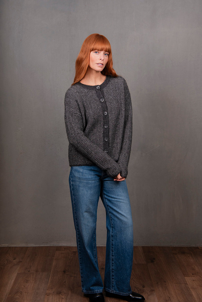 Woman wearing a dark gray cardigan and blue jeans against a plain background
