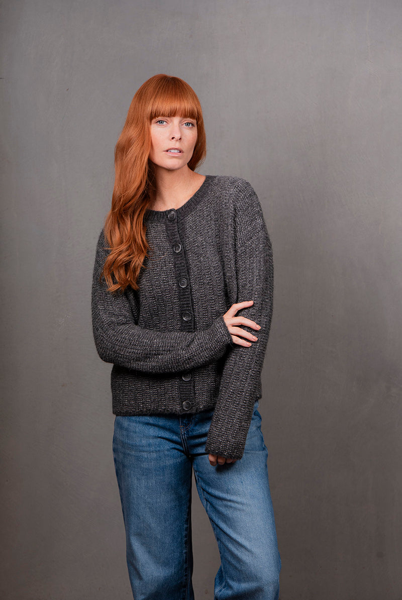 Woman wearing a gray knitted cardigan and blue jeans against a gray background