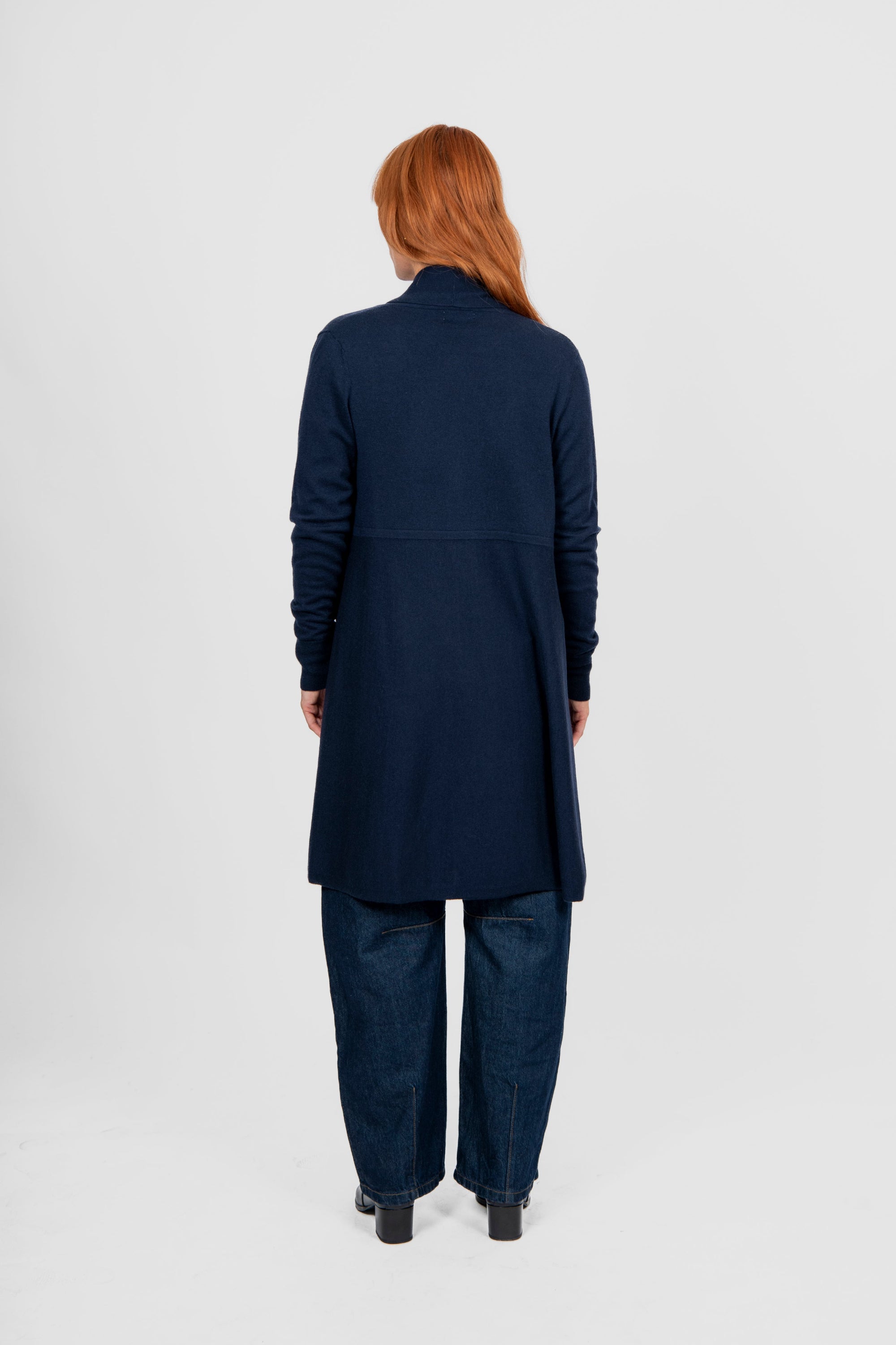 Person wearing a navy long cardigan and pants on a white background back angle