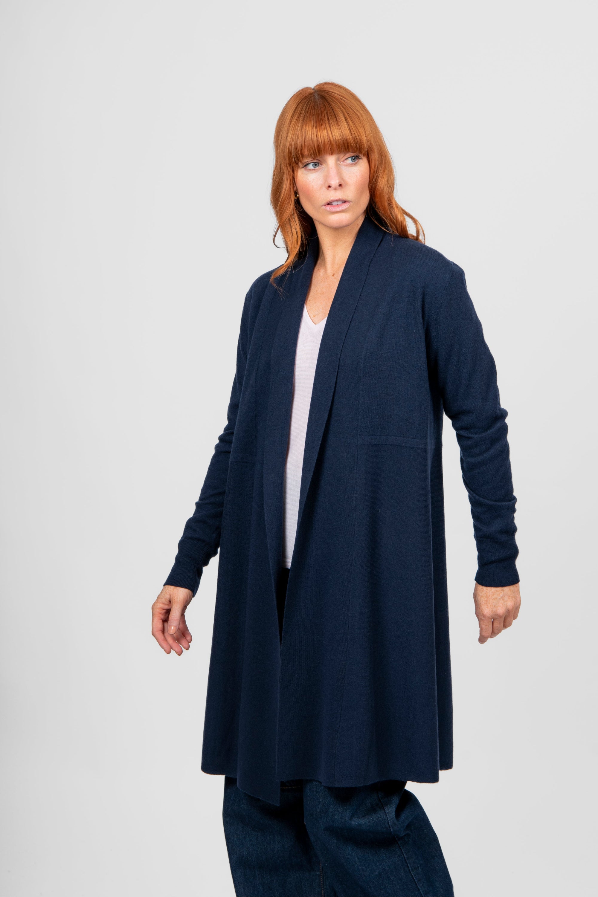 Woman wearing a long navy cardigan over a white top on a light gray background