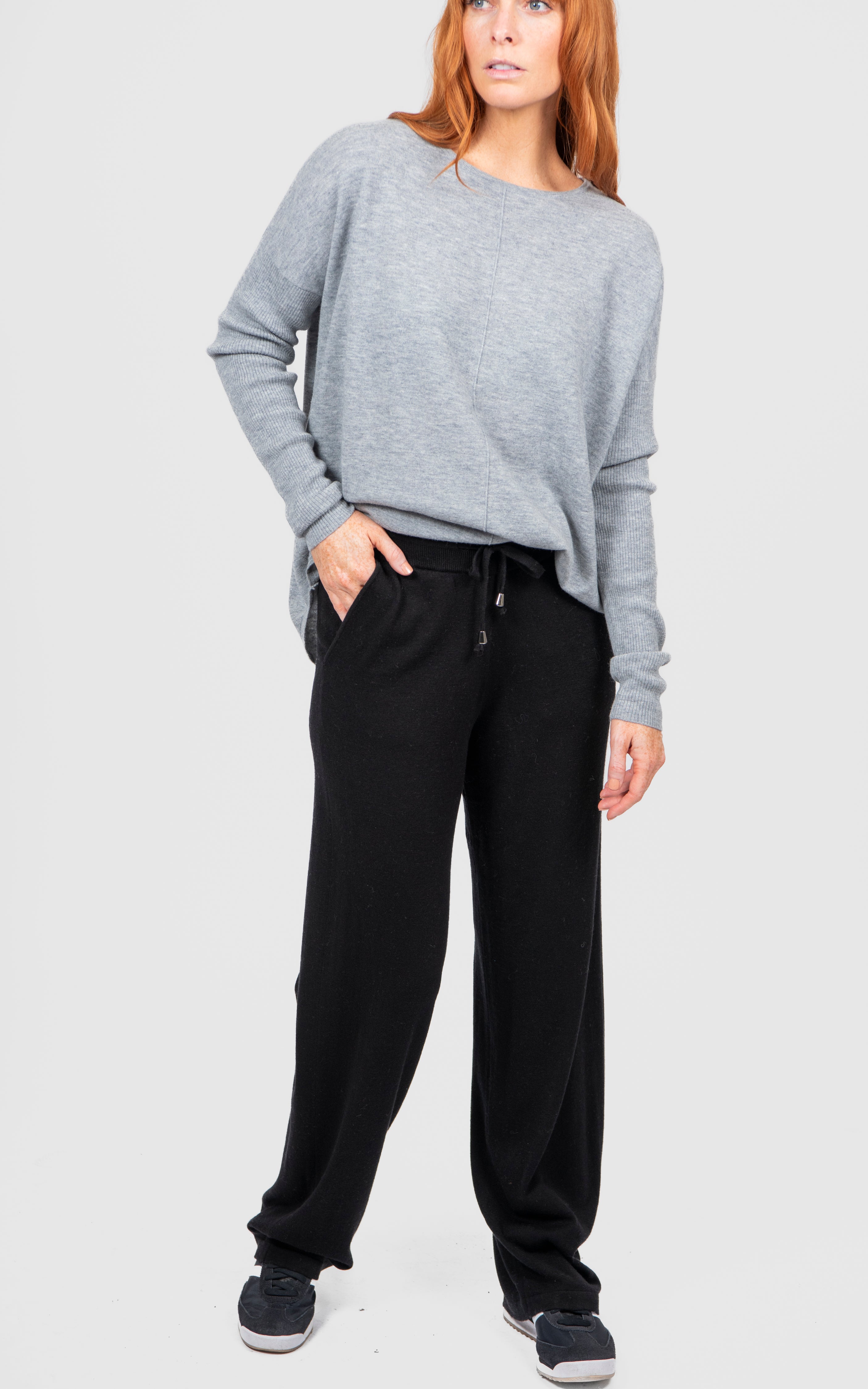 Woman wearing a gray sweater and black pants on a white background