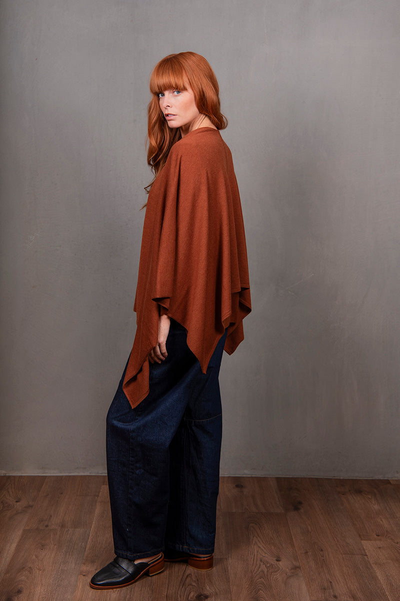 Person wearing a brown poncho over a dark outfit against a gray background