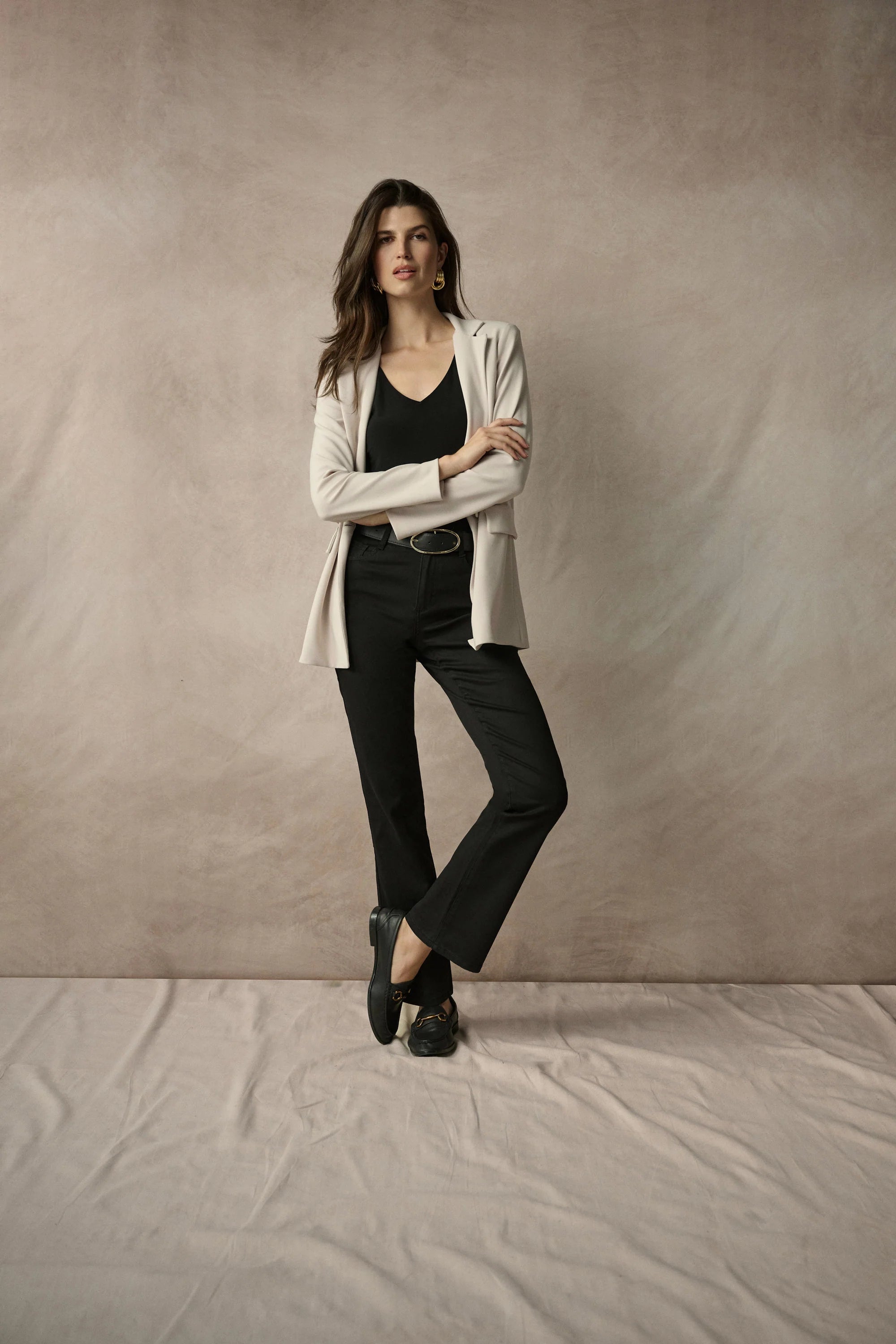Woman wearing a white blazer over a black top and pants against a plain background