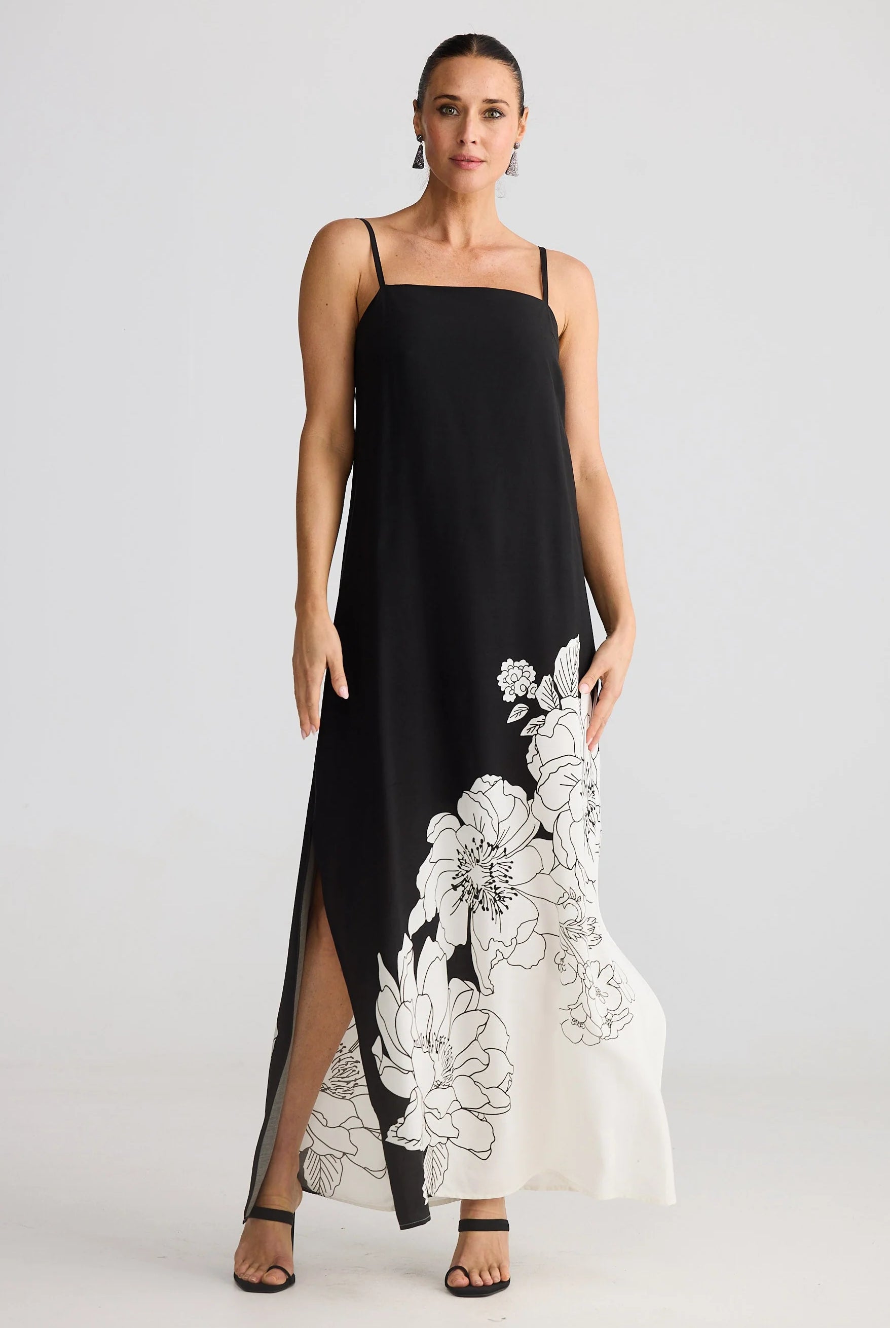Woman wearing a black slip dress with white floral embroidery on a plain background