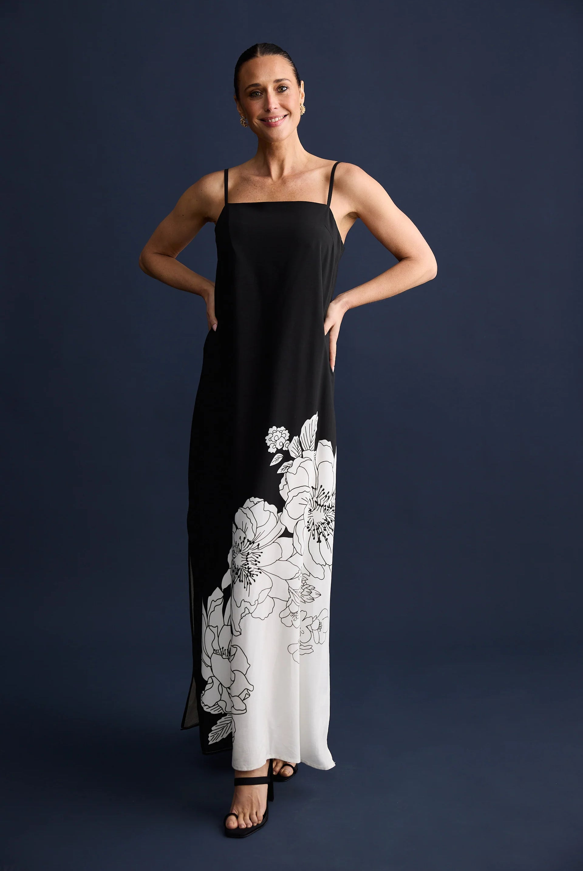 Woman wearing a black slip dress with white floral embroidery on a dark blue background