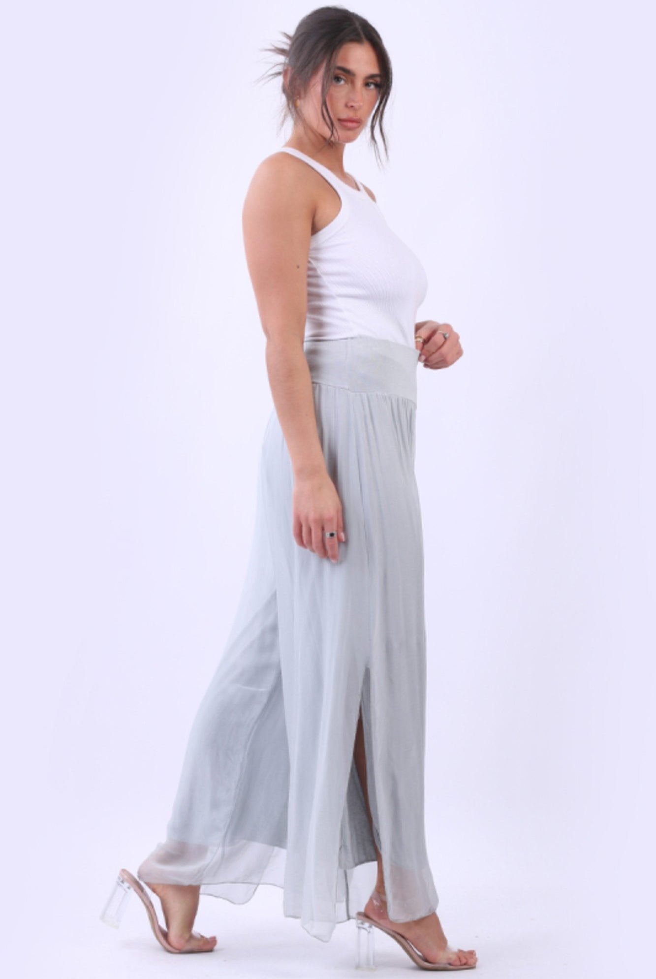 Woman wearing a white top and light gray flowing pants on a white background