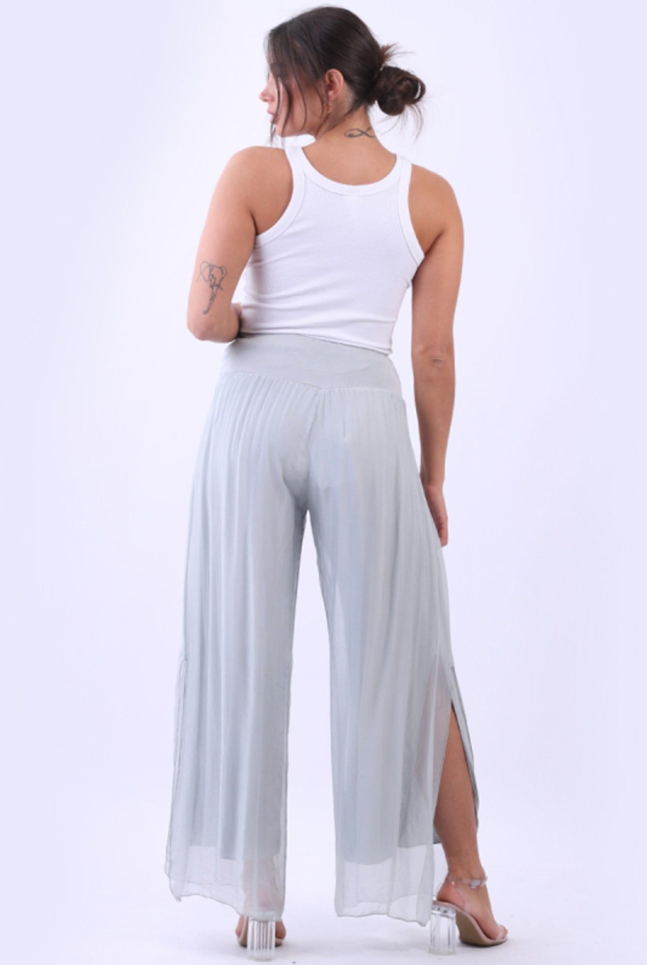 Woman wearing a white tank top and light gray wide-leg pants on a white background