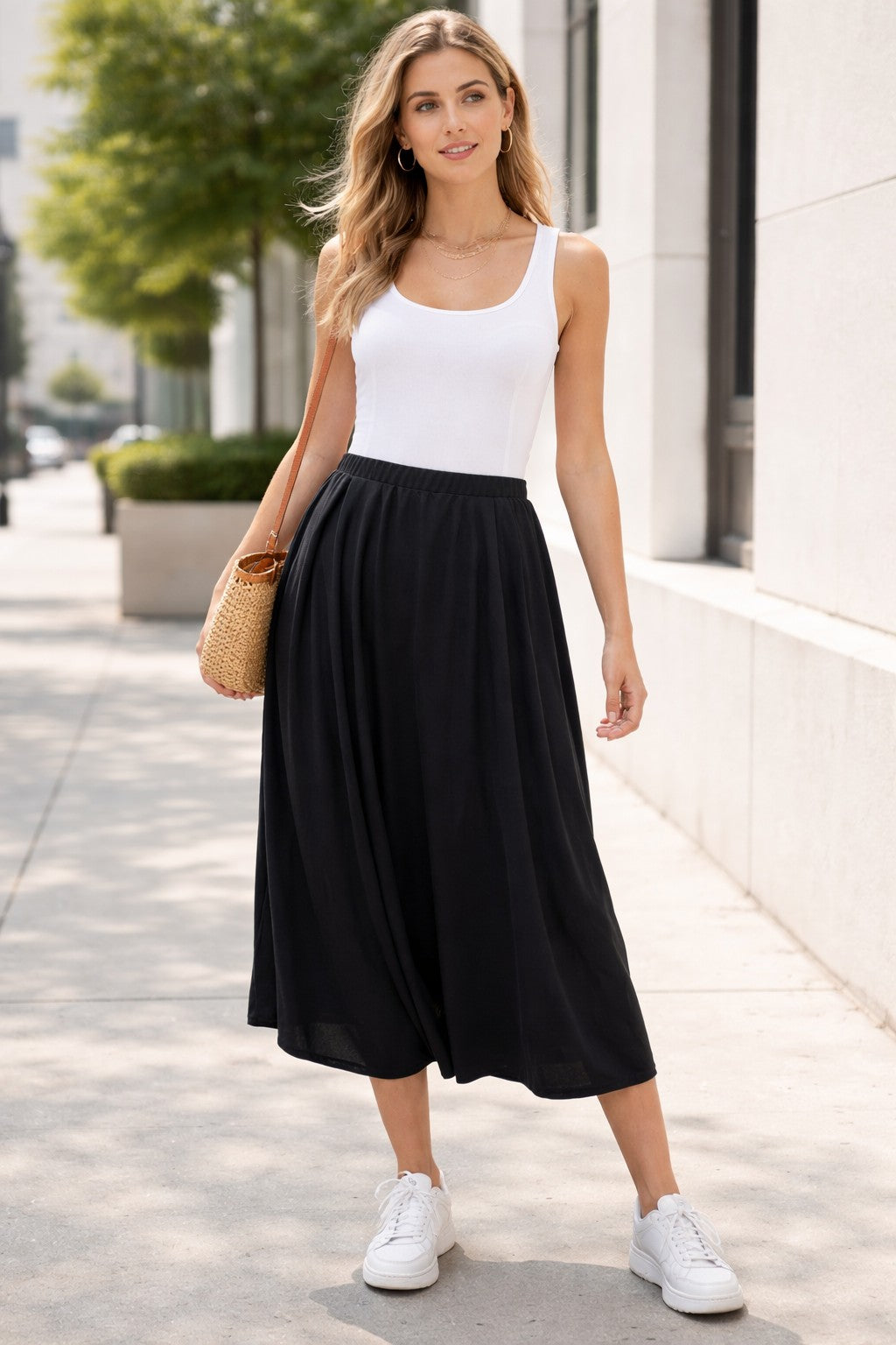 Woman wearing a white tank top and black pants on a city street.