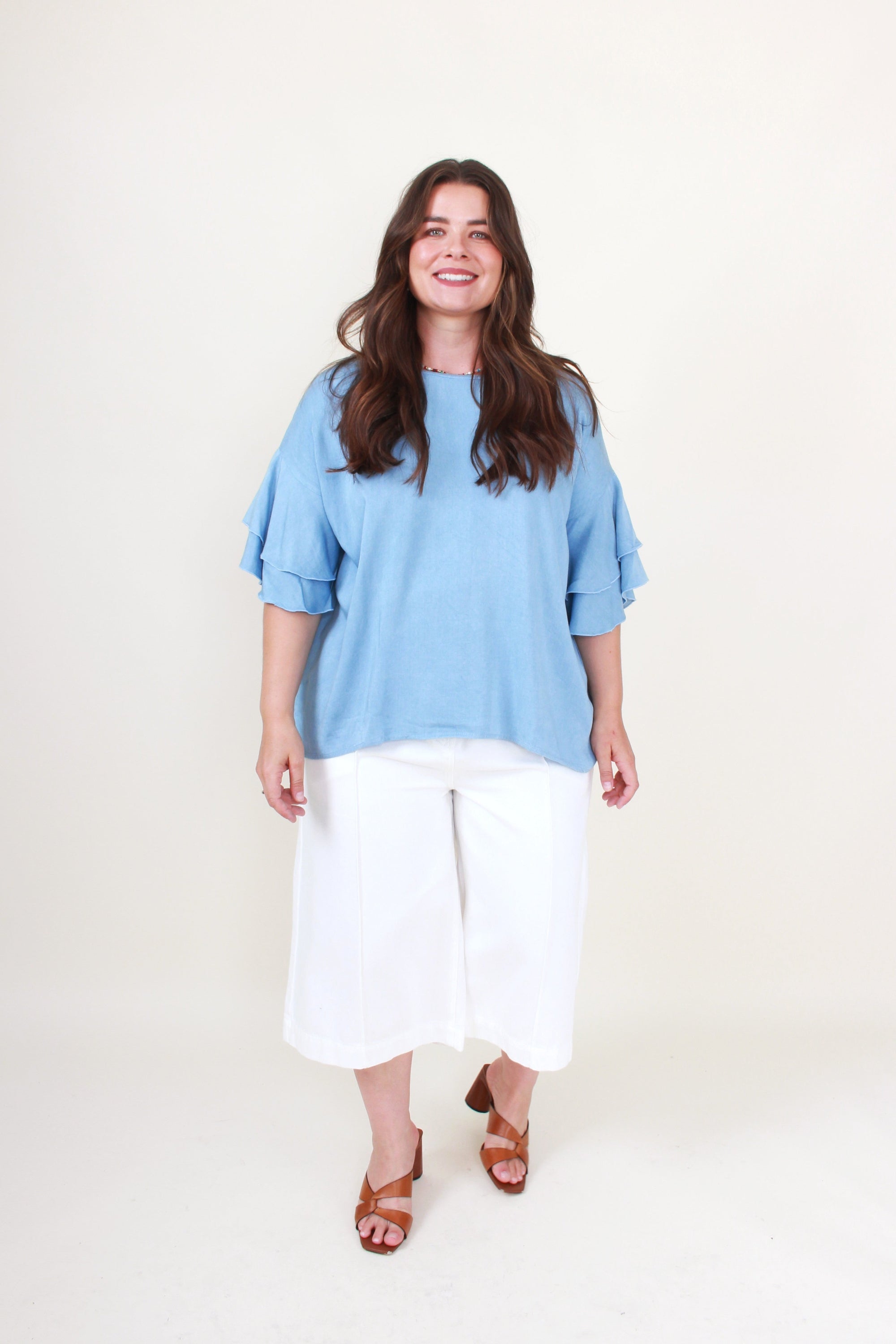 Woman wearing a light blue top and white pants on a white background