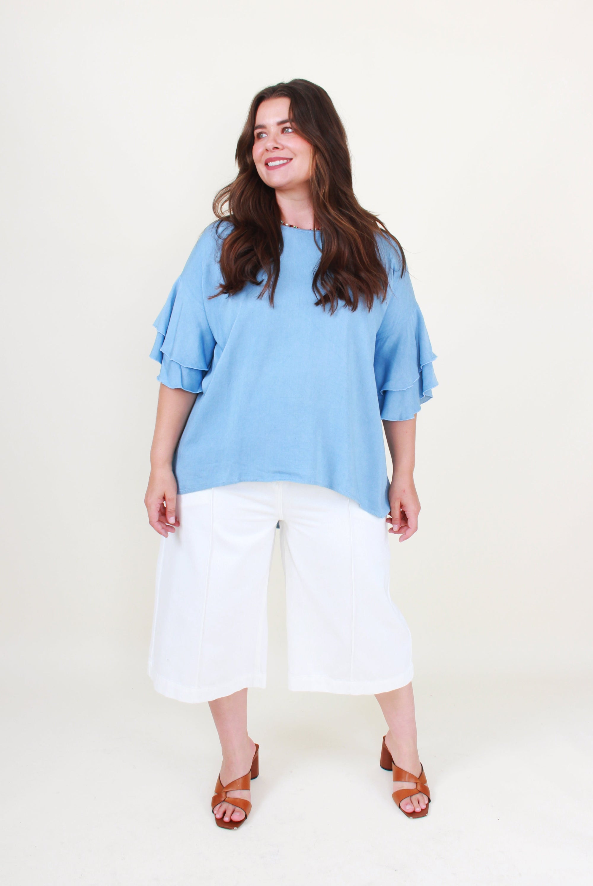Woman wearing a blue top and white pants on a plain background