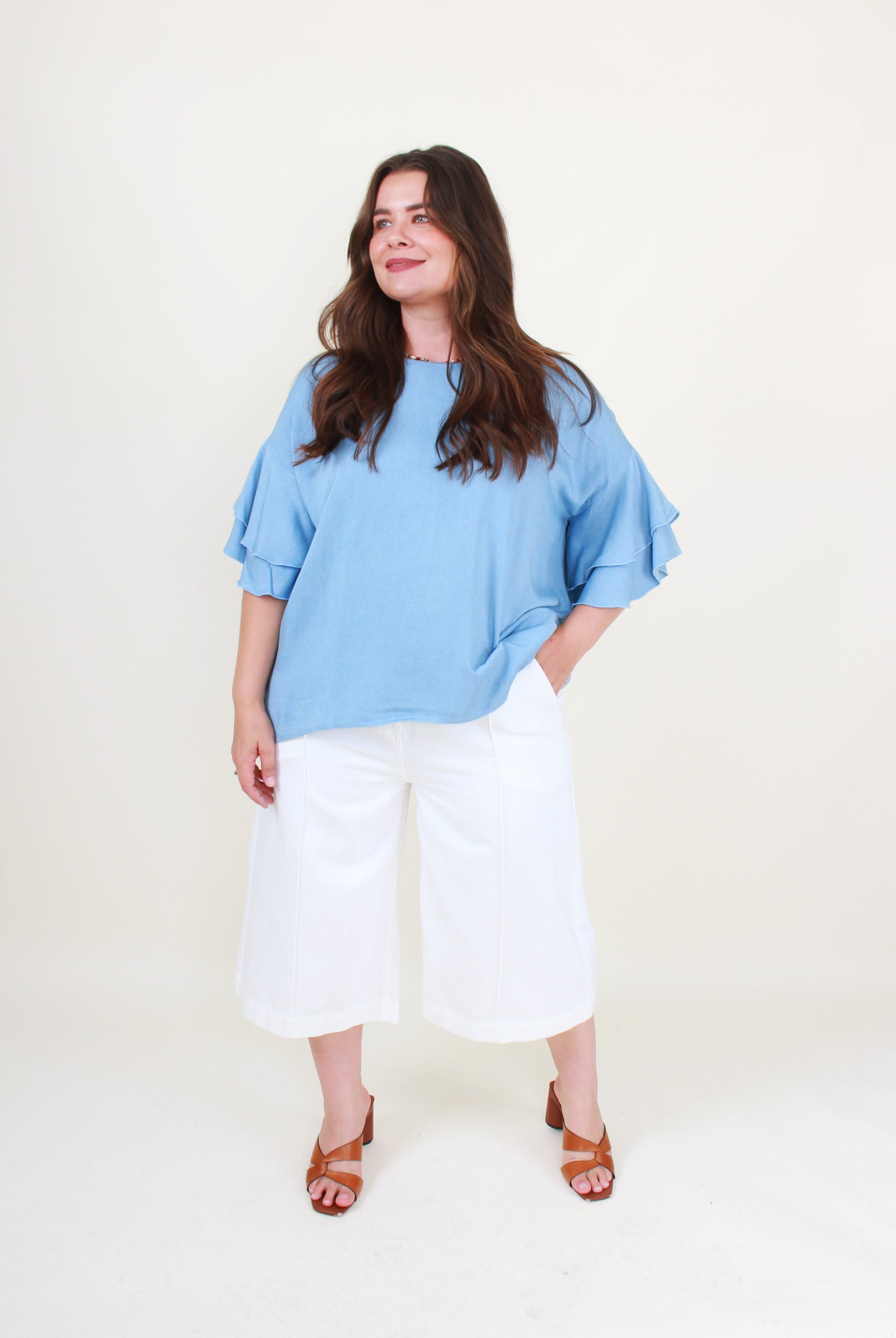 Woman wearing a blue top and white pants on a white background