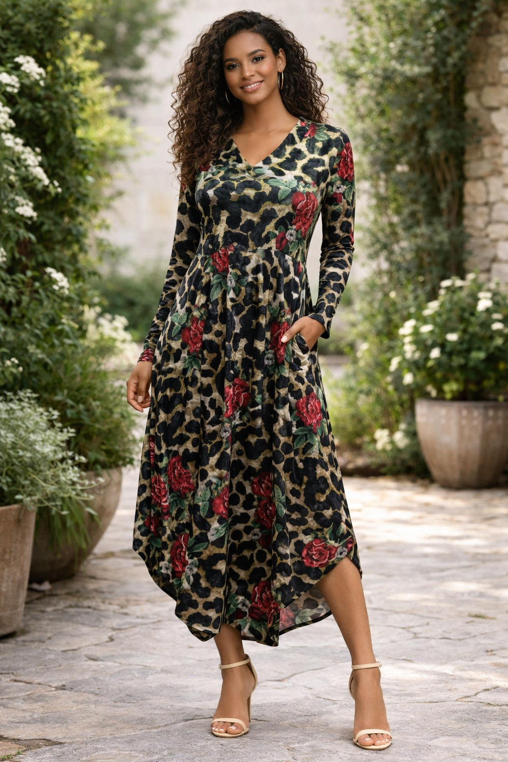 Woman wearing a long floral dress in an outdoor setting with plants and stone pavement.