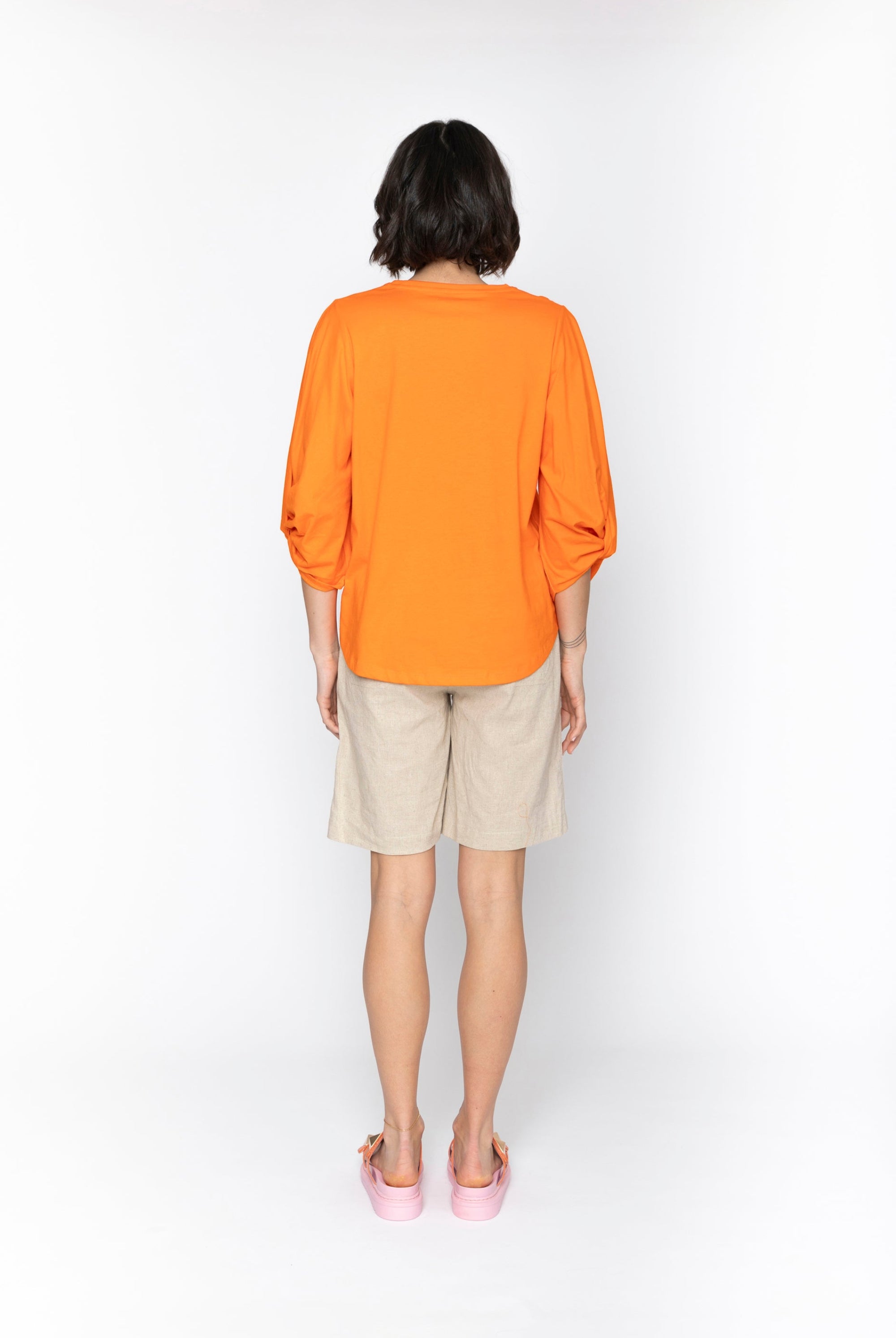 Person wearing an orange shirt and beige shorts on a white background