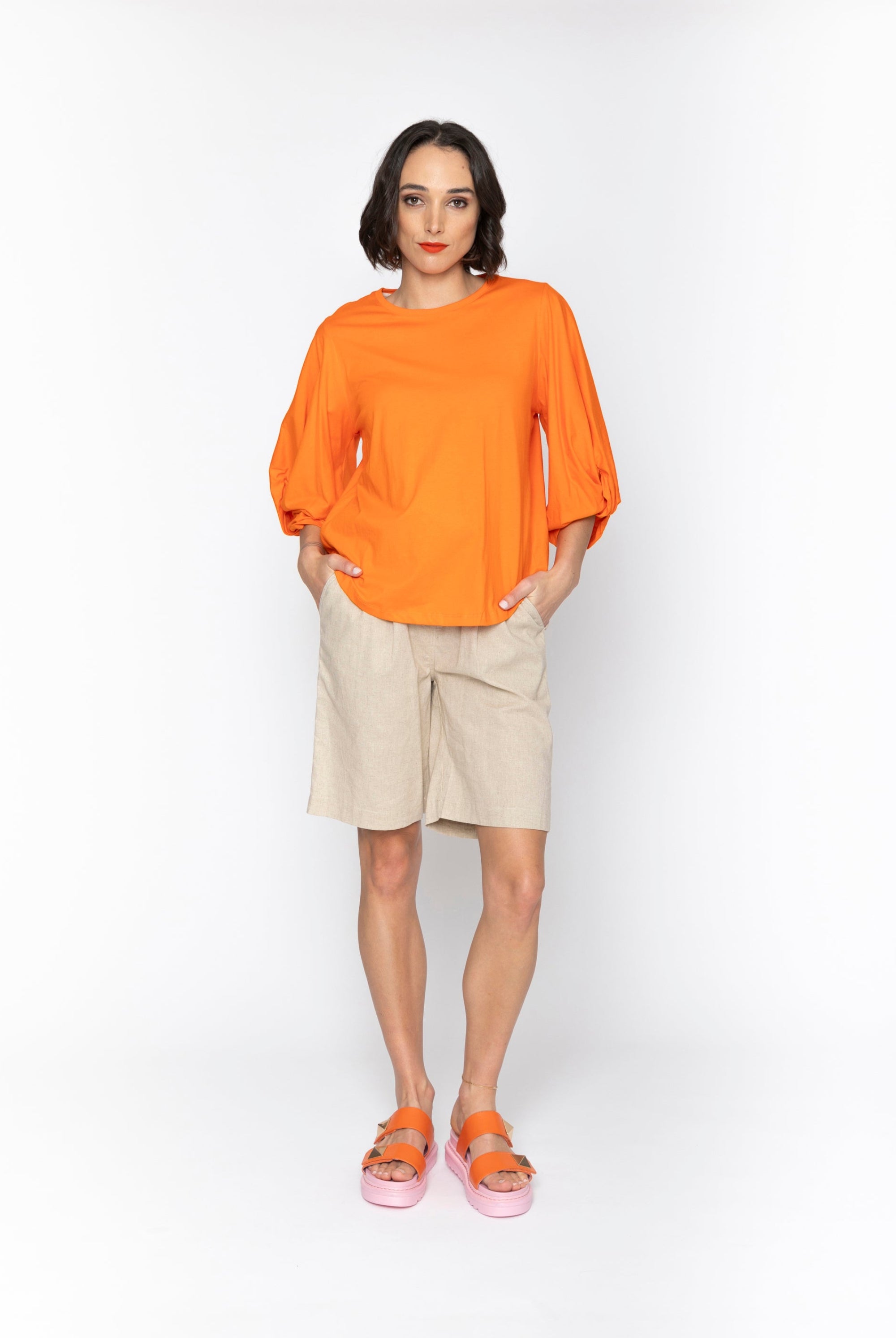 Woman wearing an orange top and beige shorts on a white background