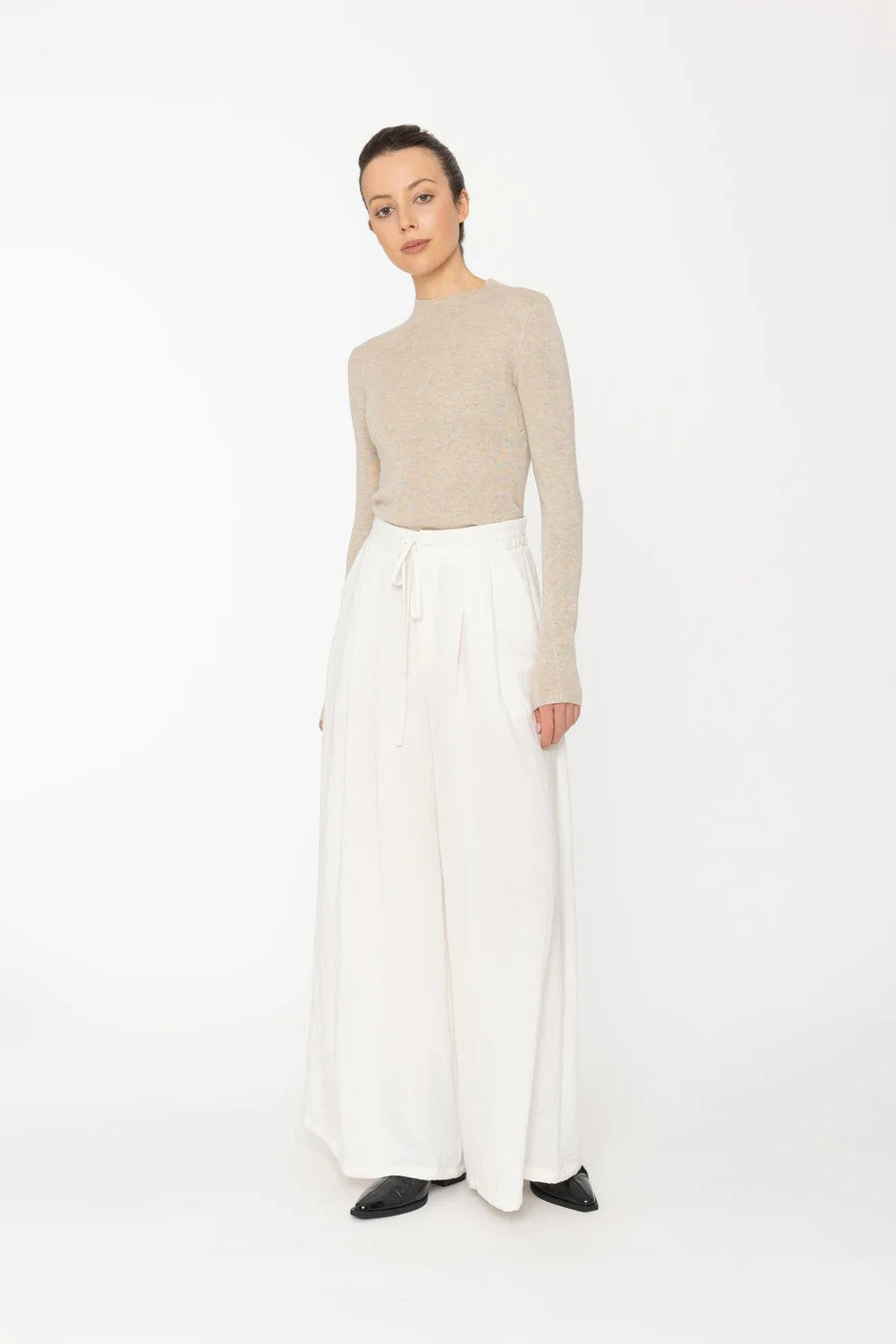 Person wearing a beige sweater and white pants on a white background