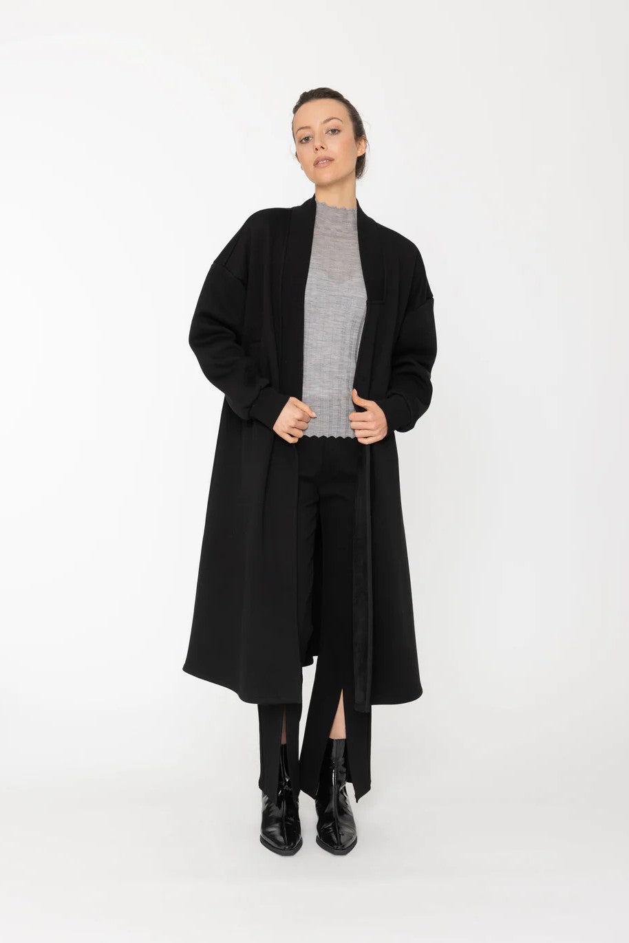 Person wearing a black coat over a gray sweater on a white background