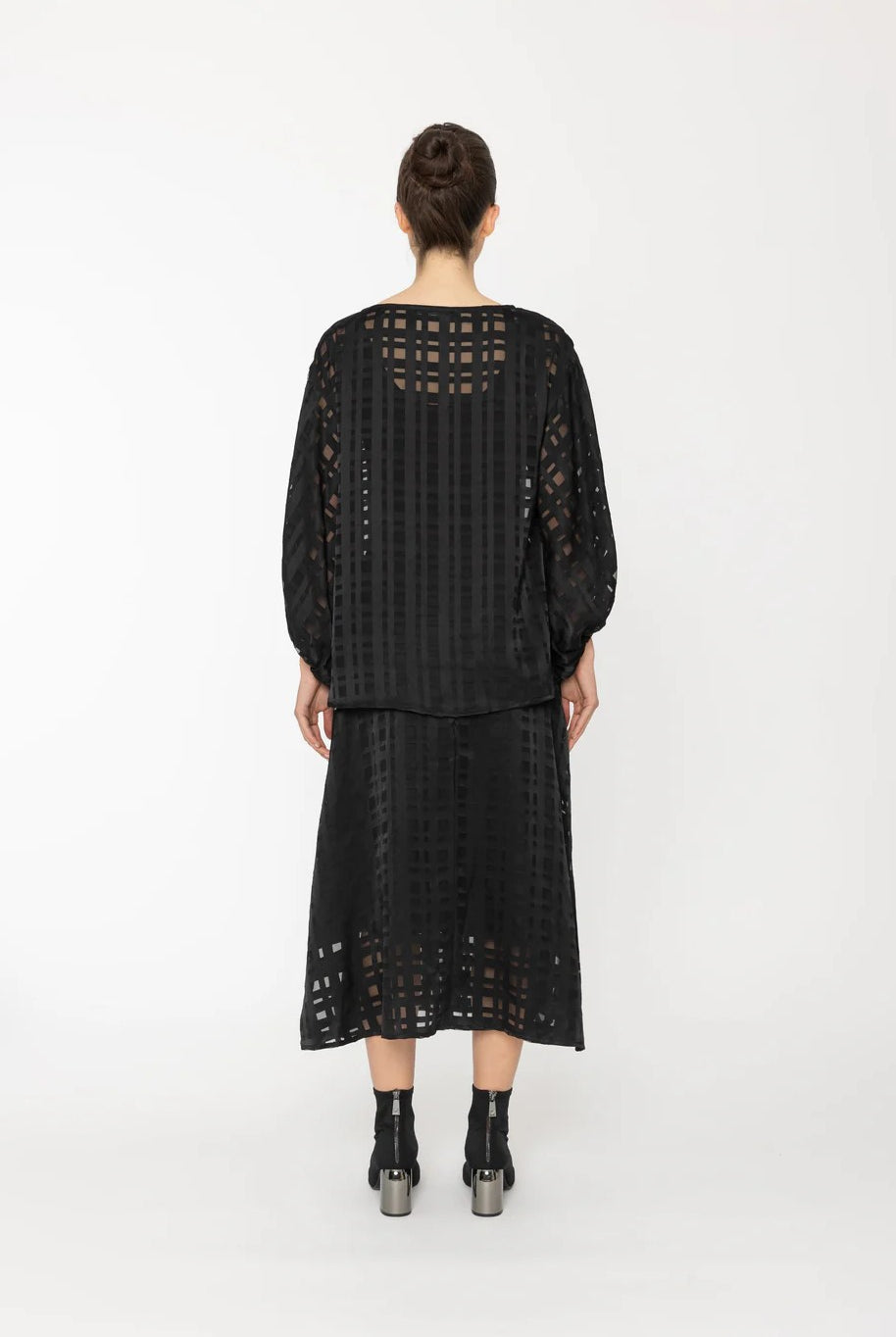 Person wearing a black outfit with lace details on a white background back angle