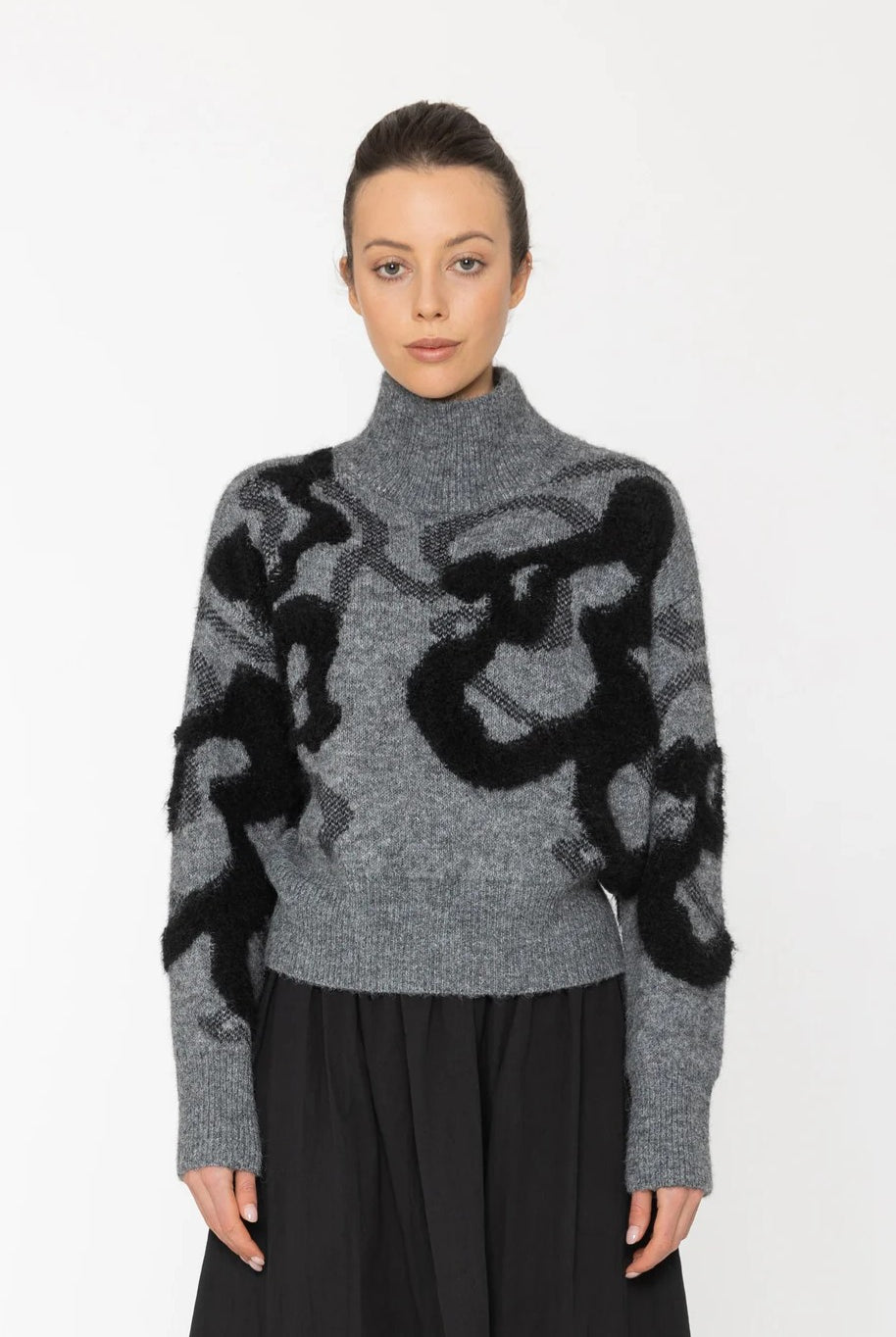 Woman wearing a gray sweater with black abstract patterns on a white background