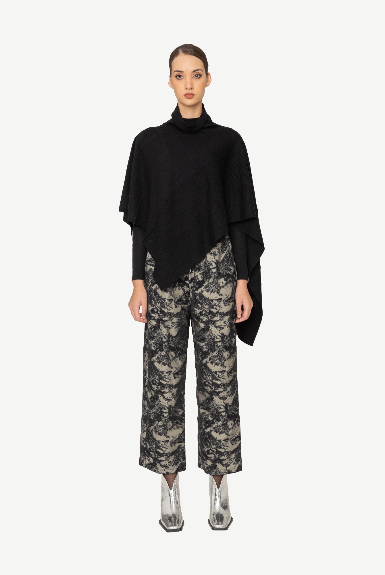 Woman wearing a black sweater and patterned pants on a white background