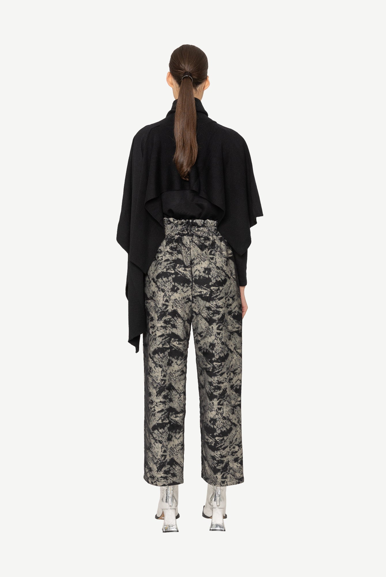 Person wearing a black top and patterned pants on a white background back angle