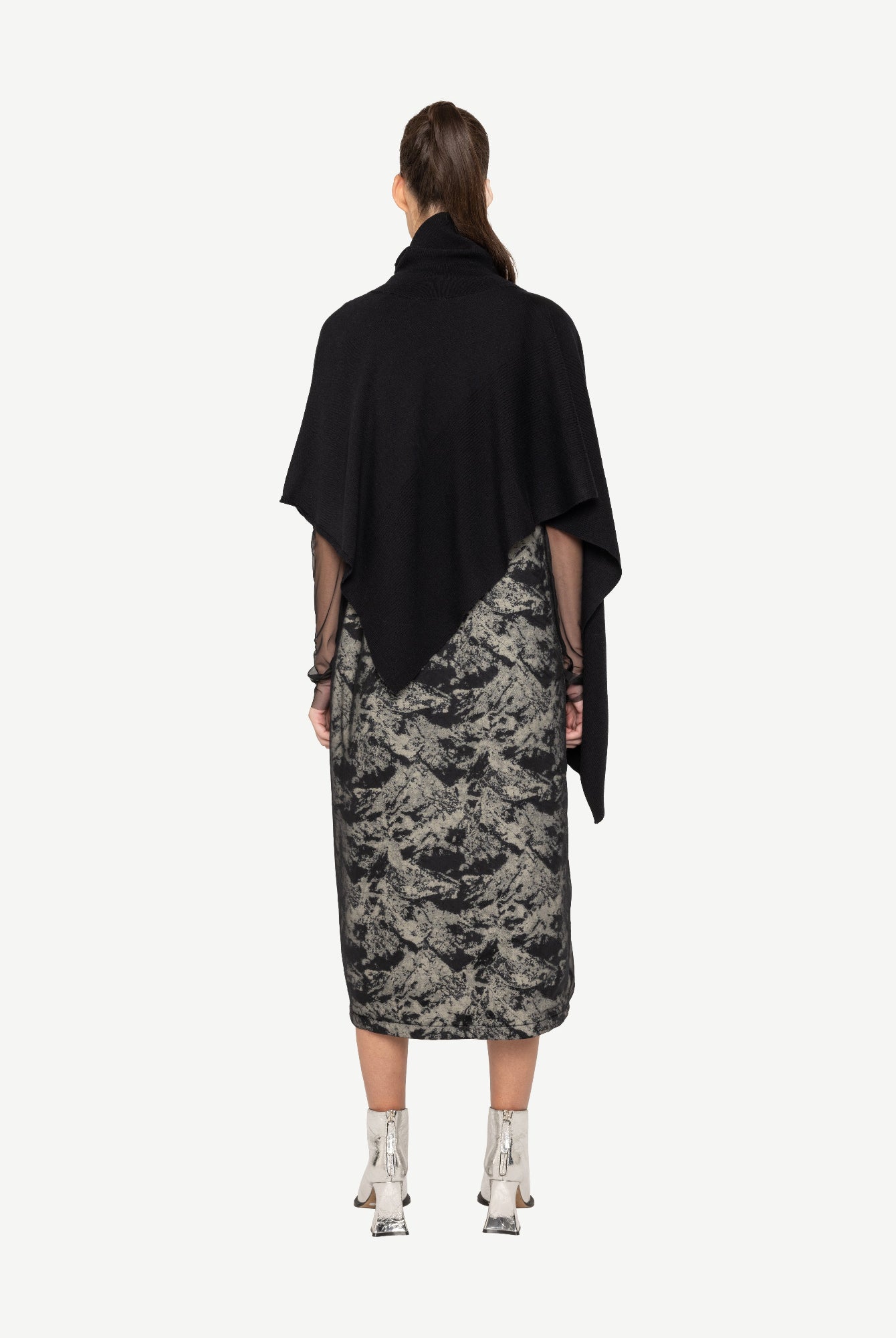 Woman wearing a black top and patterned skirt on a white background back angle