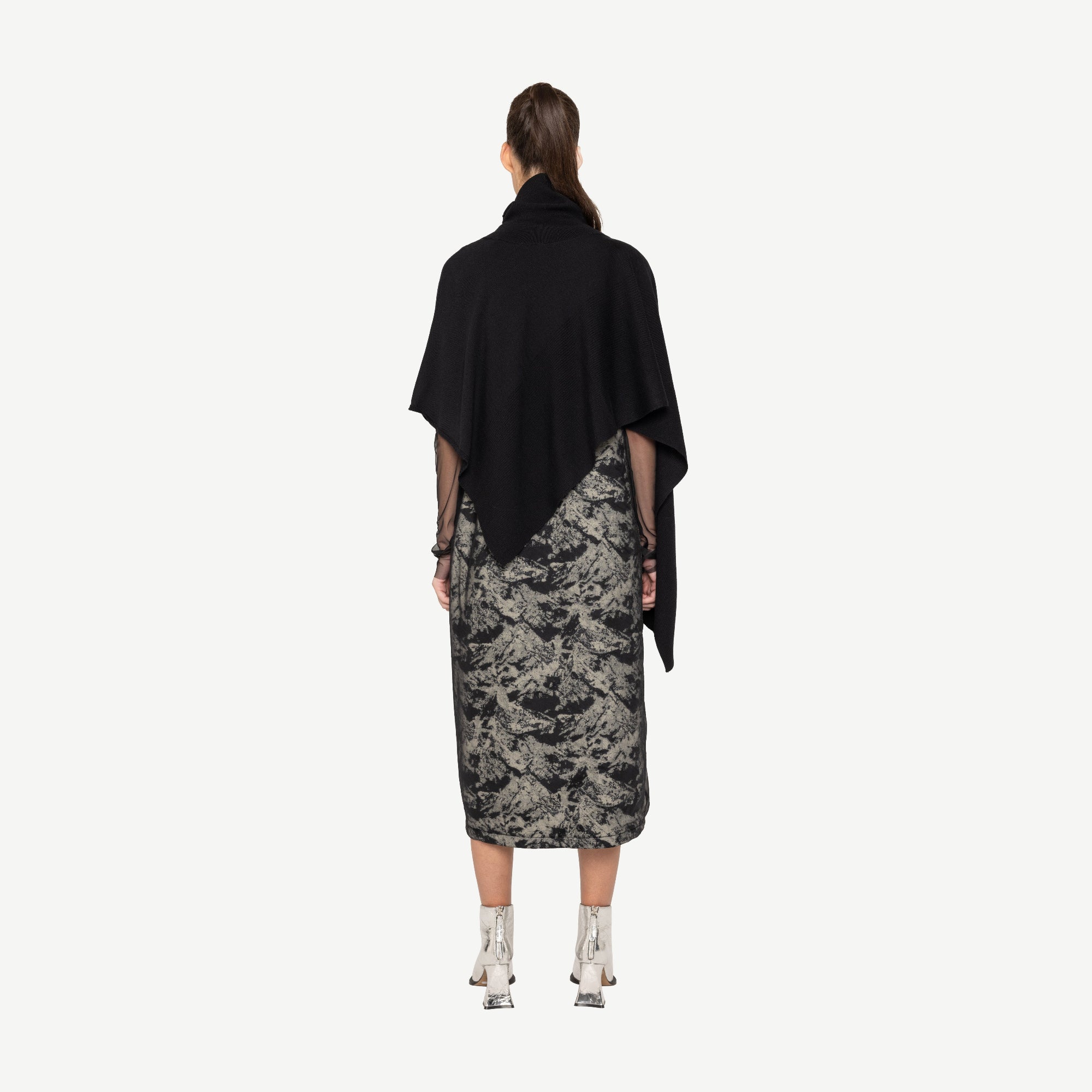 Woman wearing a black top and patterned skirt on a white background back angle