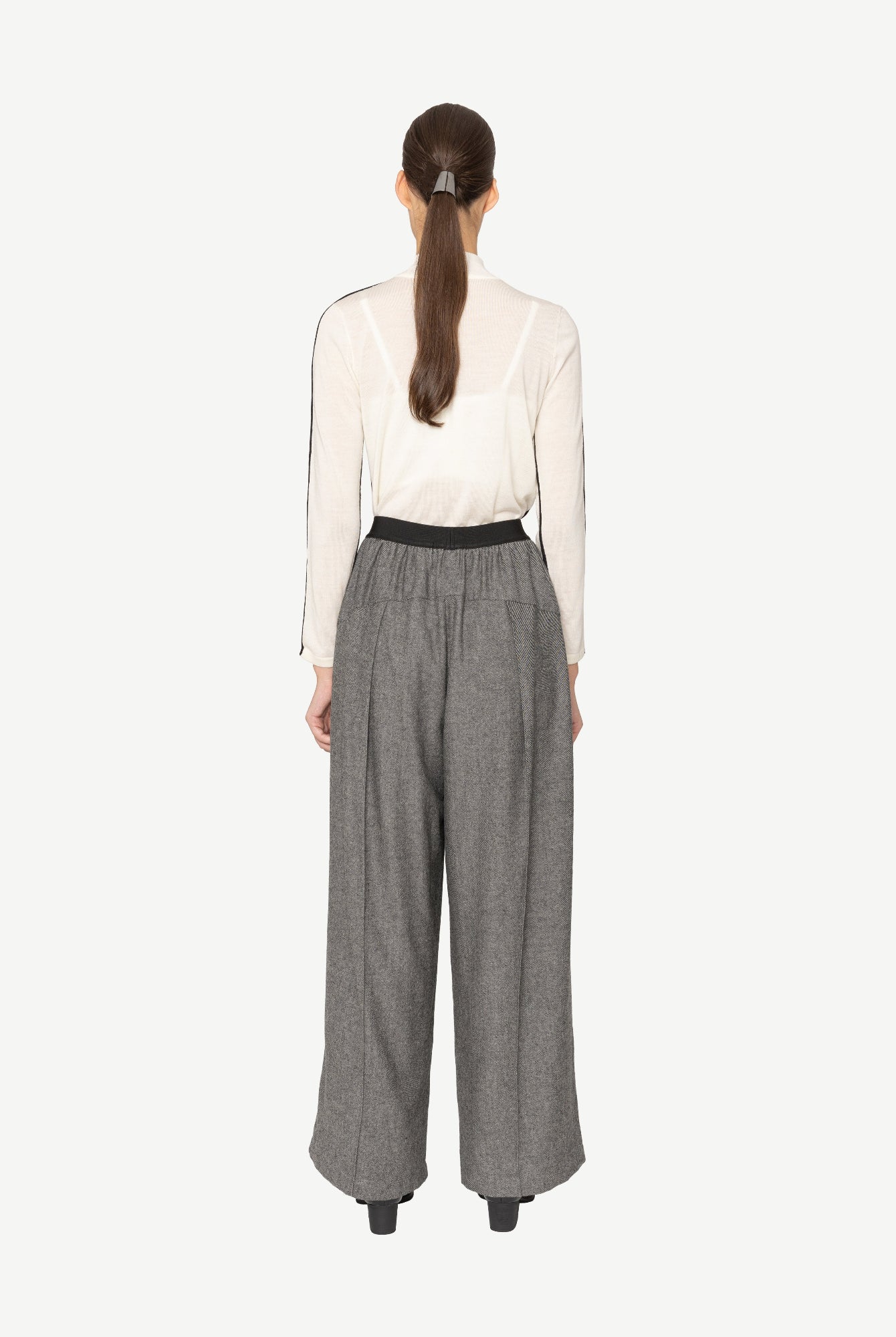 model wearing white top and grey wide leg pants on white background back angle