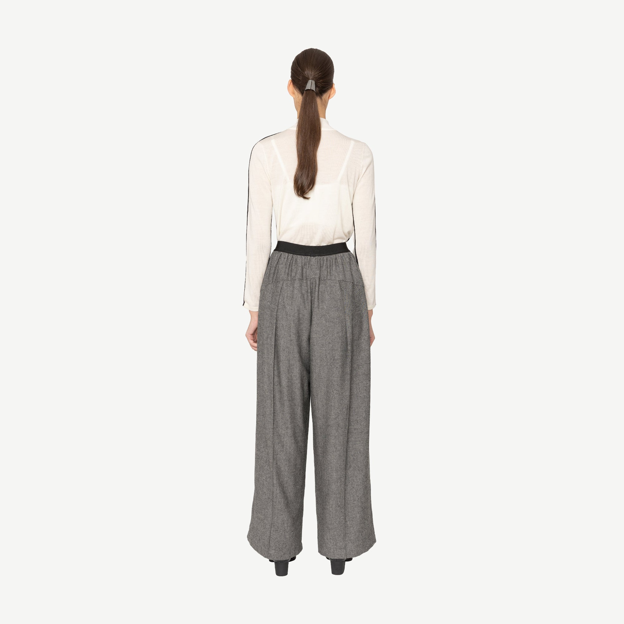 model wearing white top and grey wide leg pants on white background back angle