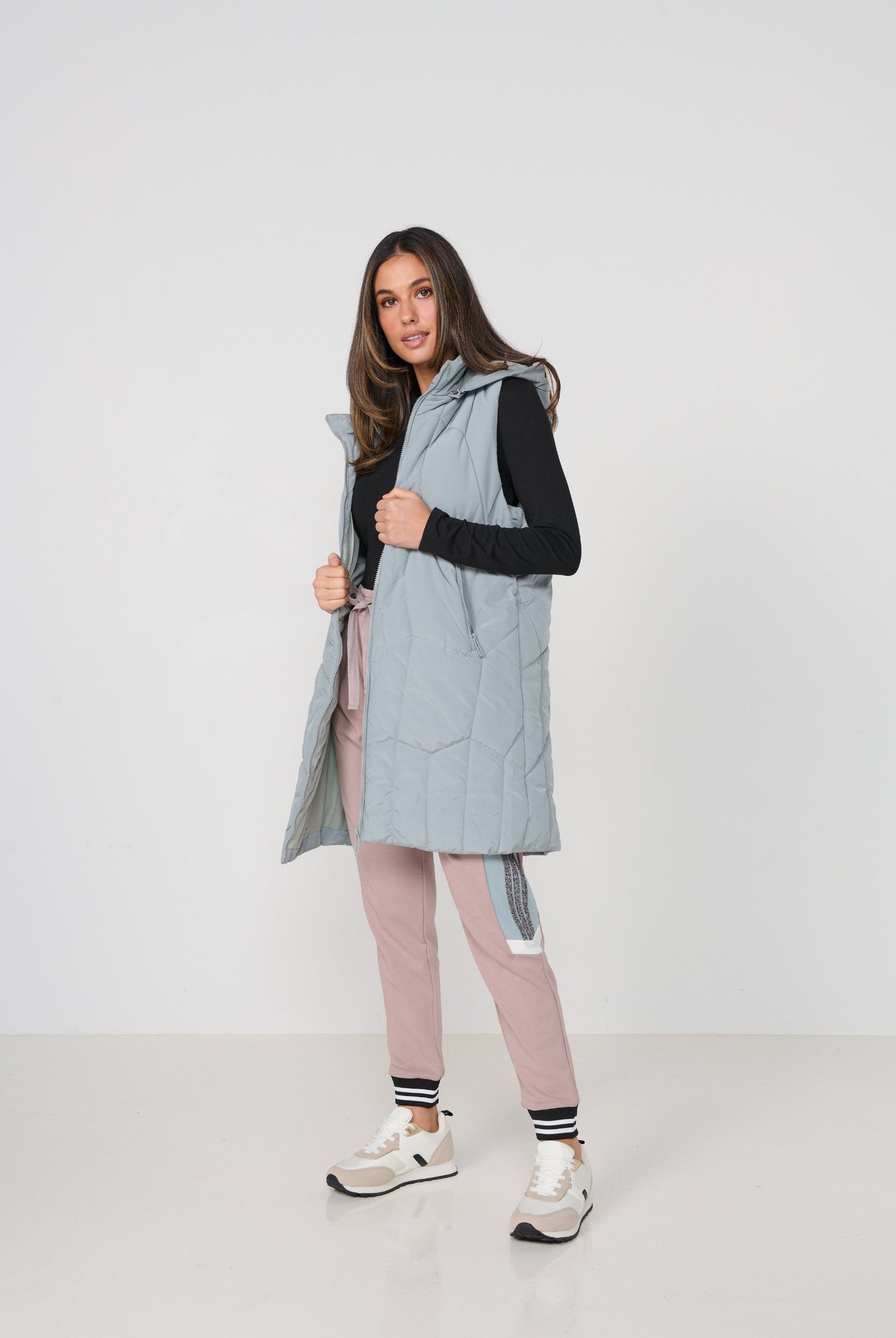 Woman wearing a light gray puffer vest over a black top with pink leggings on a white background