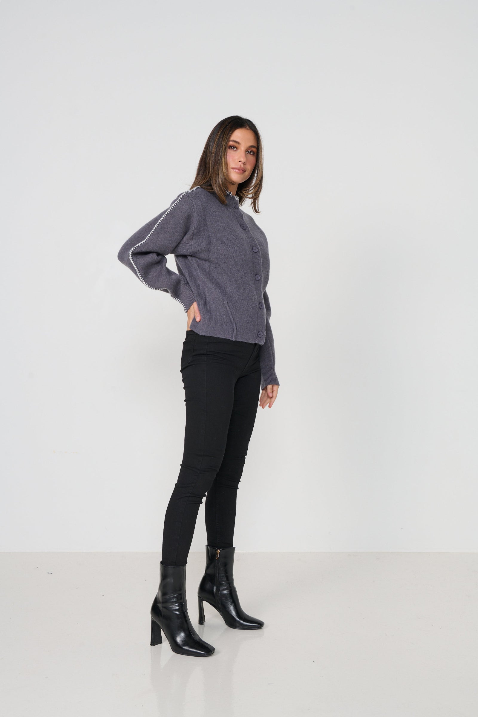 Woman wearing a gray cardigan and black pants with black boots on a white background