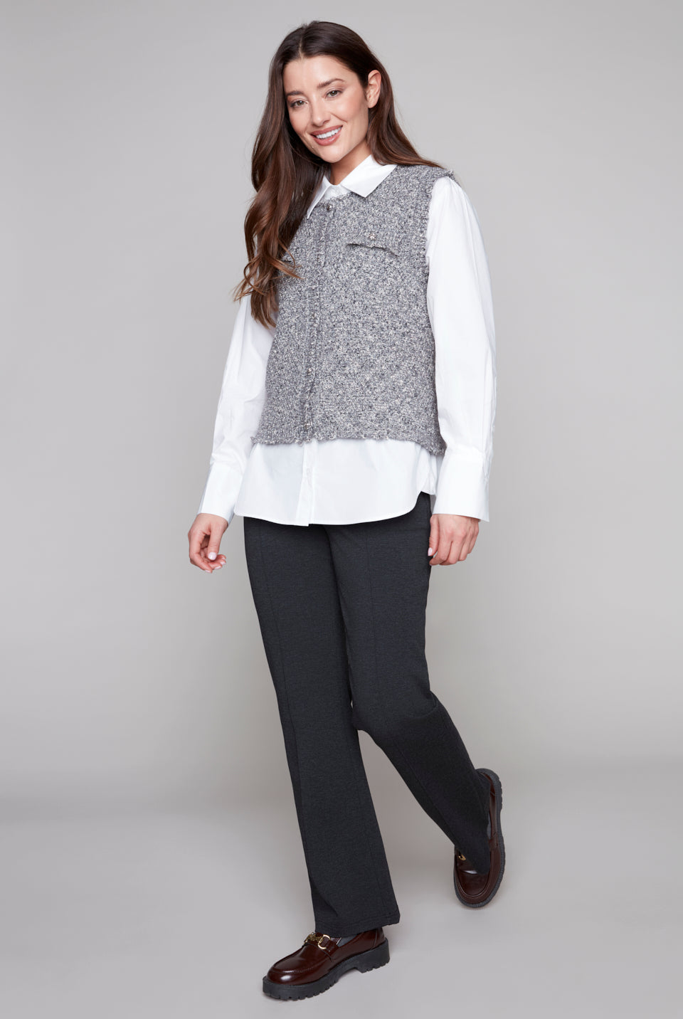 Woman wearing a white shirt, gray vest, black pants, on a gray background